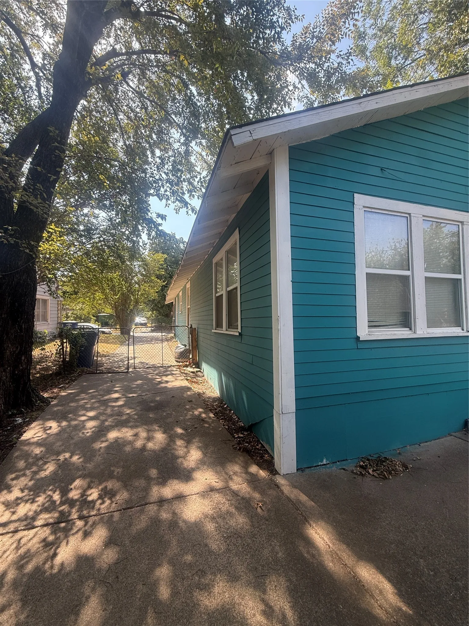Teal horizontal siding with white trim, multiple windows, concrete walkway, and chain-link fencing