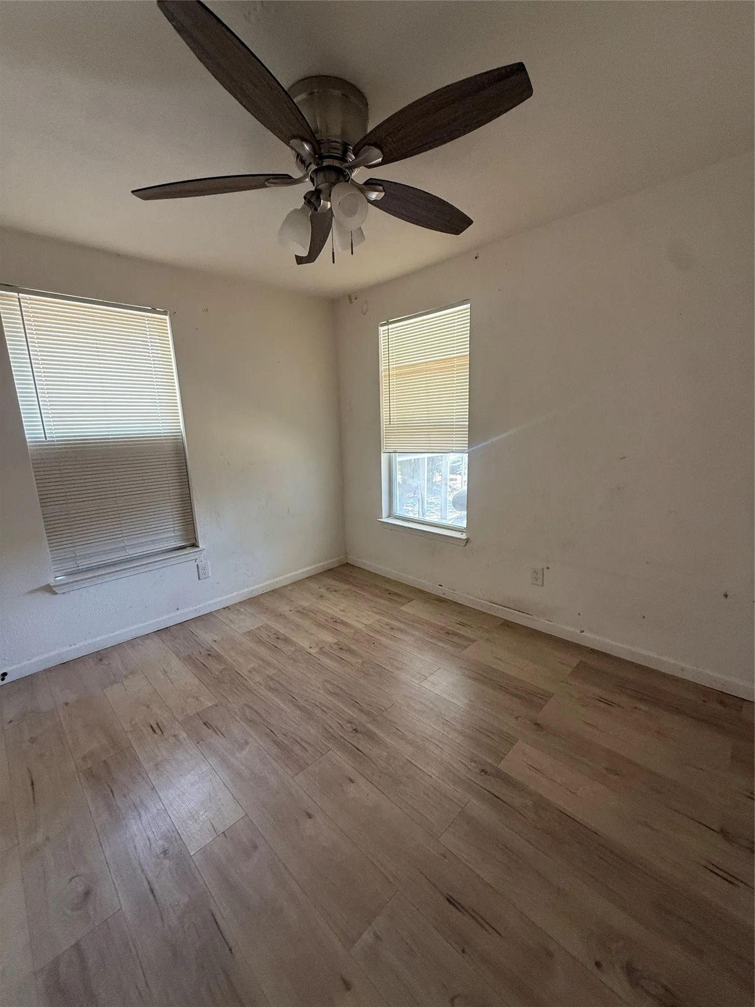 Wood-finish flooring, two windows with blinds, and a ceiling fan with integrated lighting