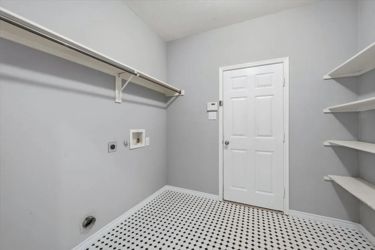 Laundry area featuring black and white patterned flooring, built-in shelving, and a clothing rod