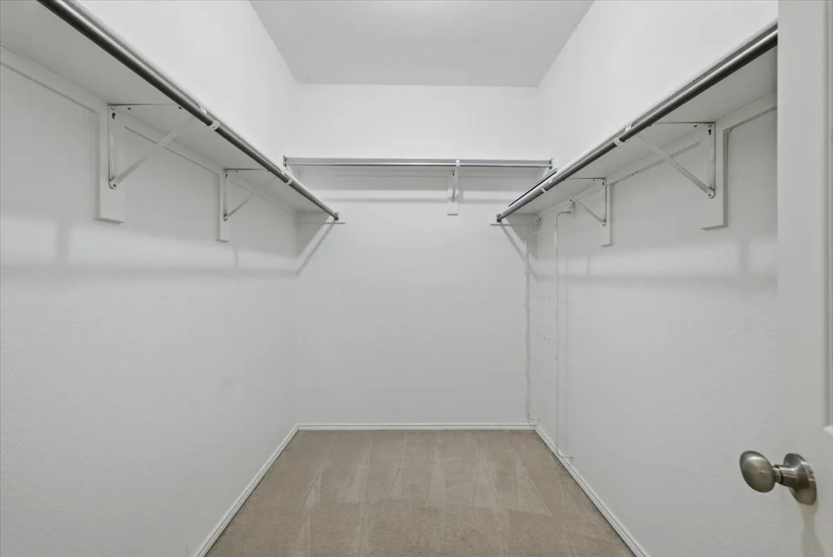 Spacious walk-in closet featuring dual clothing rods with sturdy metal brackets, polished concrete flooring, and bright overhead lighting for optimal visibility and organization