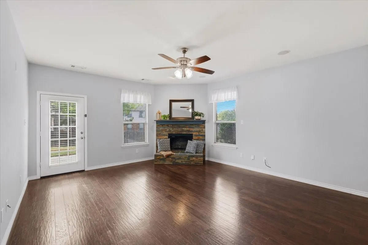 Wood-finish flooring, corner fireplace with stone surround, ceiling fan, and transom windows