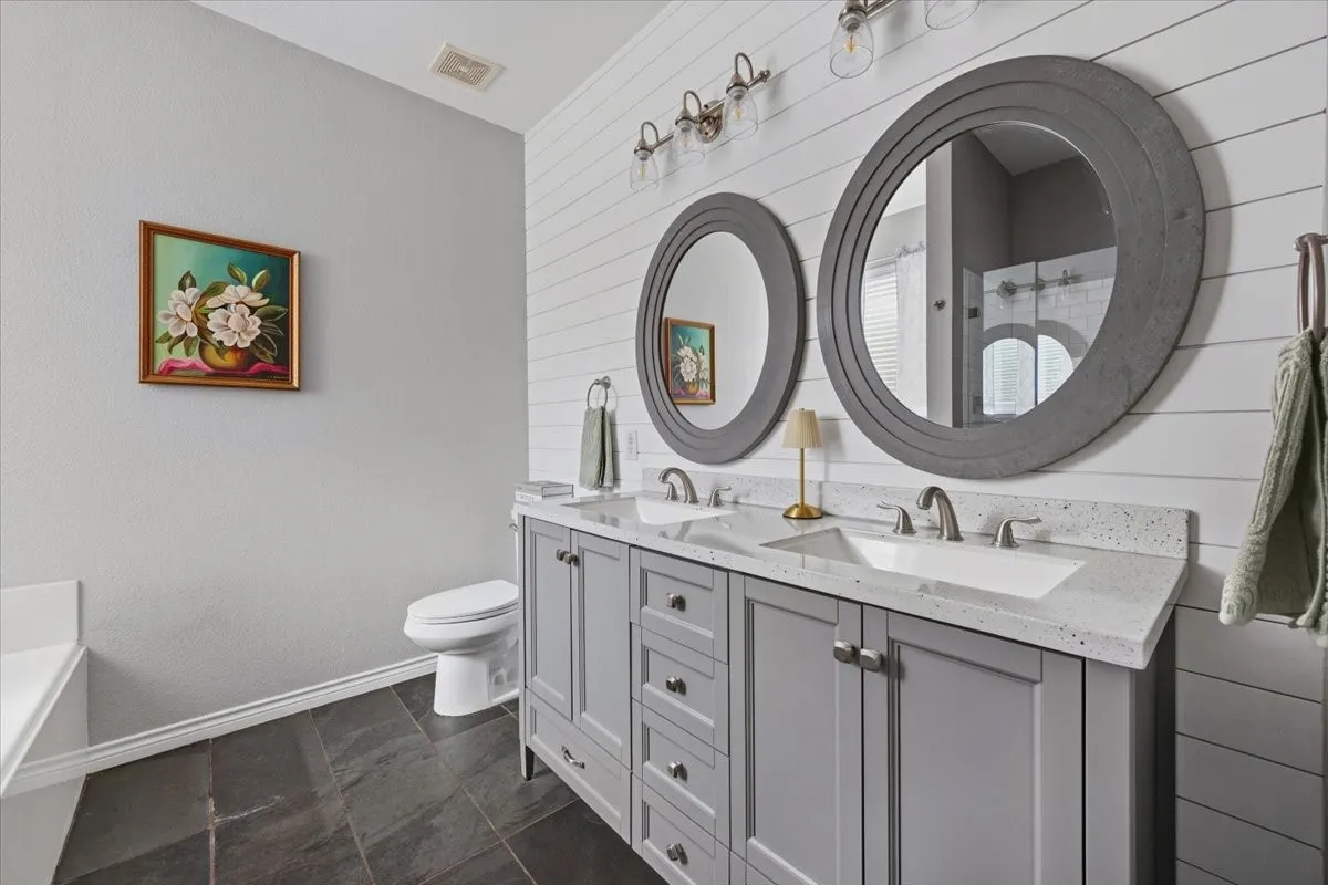Double vanity with gray cabinetry, white countertops, dual undermount sinks, and two circular framed mirrors