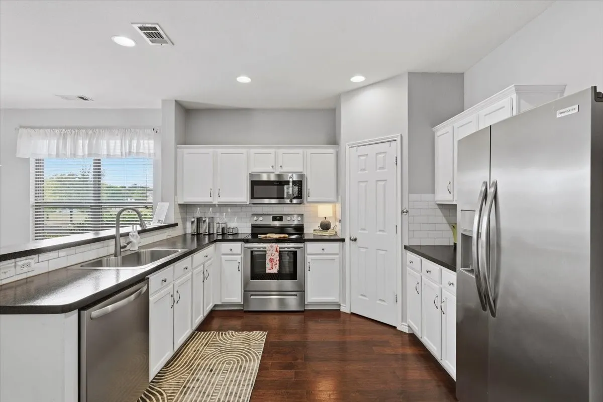 Kitchen featuring white cabinetry, dark countertops, a stainless steel appliance suite, and wood-finish flooring