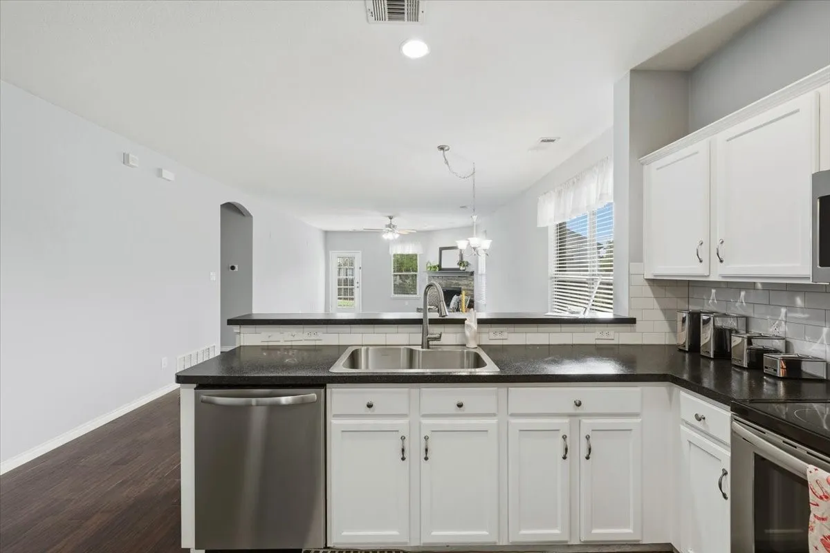 White cabinetry with dark countertops, stainless steel sink, tile backsplash, and wood-finish flooring