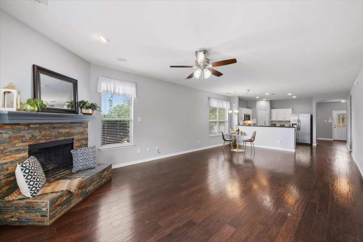 Open-concept living area with dark wood-finish flooring, a stacked stone fireplace, and light gray walls