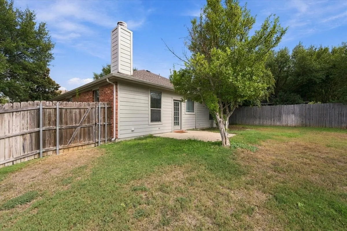 Rear elevation with a wood privacy fence, a concrete patio, and mature trees