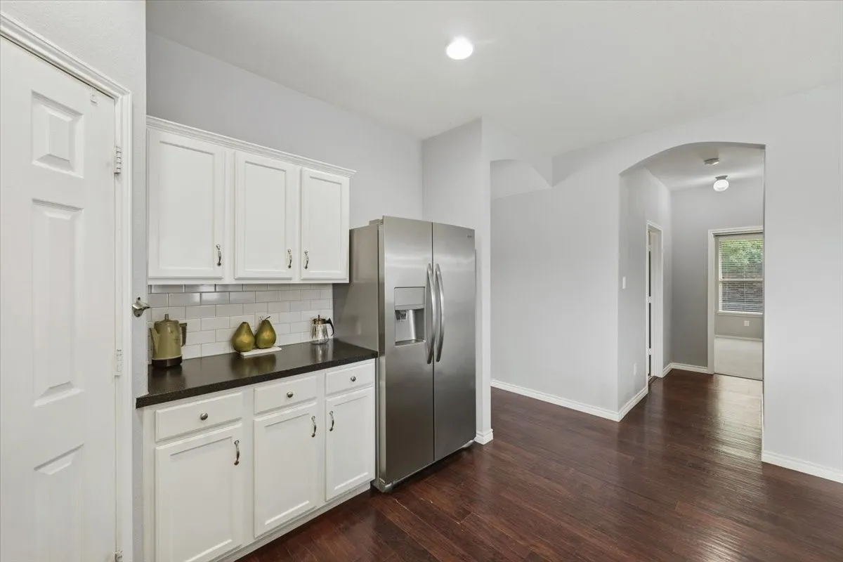 White shaker-style cabinetry with dark countertops, white subway tile backsplash, stainless steel refrigerator, and wood-finish flooring