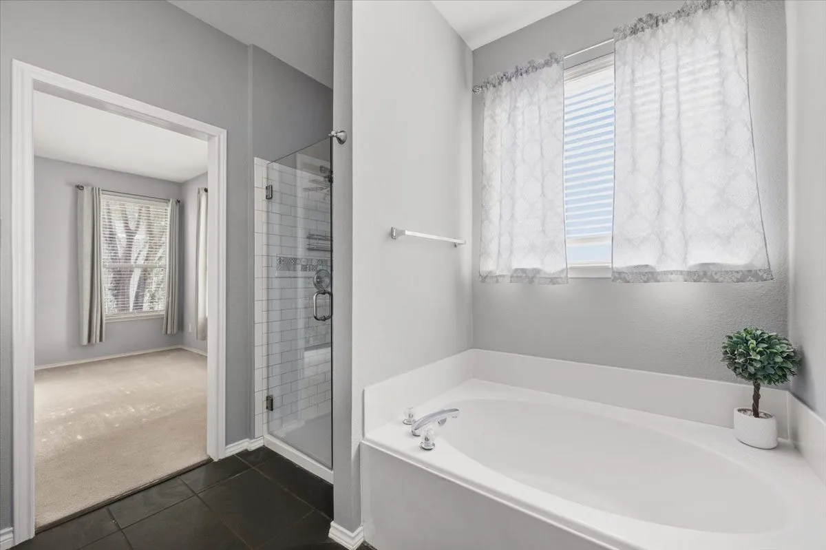 Deep soaking tub, separate glass-enclosed shower, dark tile flooring, and light-toned walls