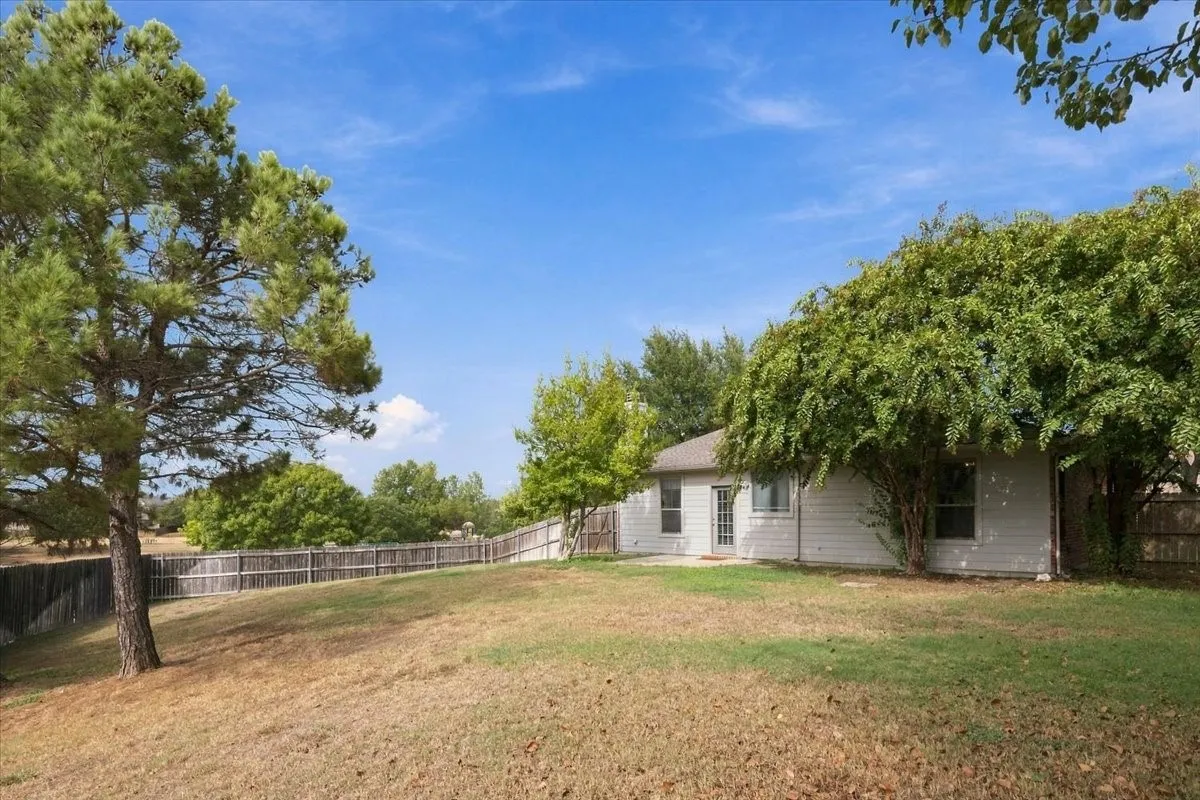 Expansive backyard with a sloped lawn, mature trees, wood fence, and a rear exterior with a door and windows