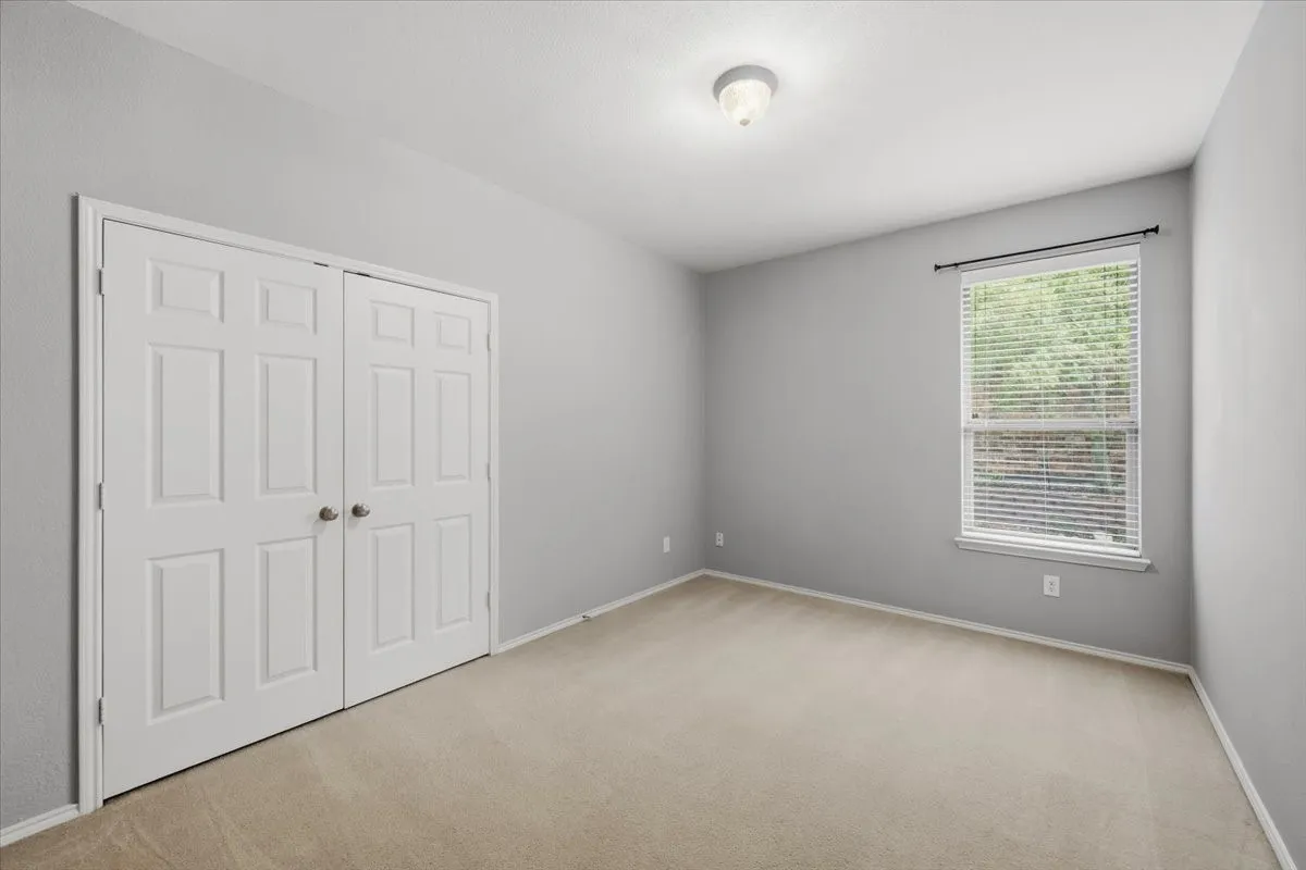 Carpet flooring, neutral painted walls, ceiling-mounted light fixture, window with blinds, and paneled bifold closet doors