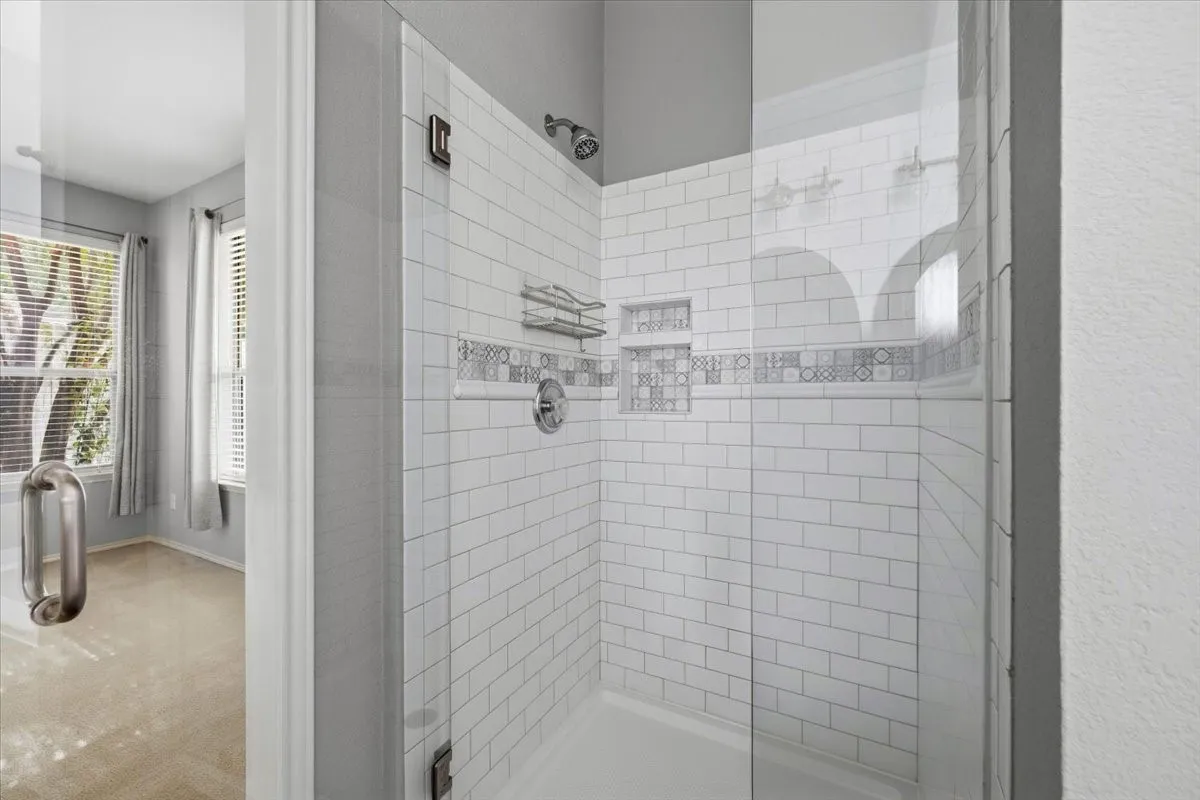 Shower enclosure with subway tile surround, decorative accent tile band, built-in shower niches, and an integrated shower caddy