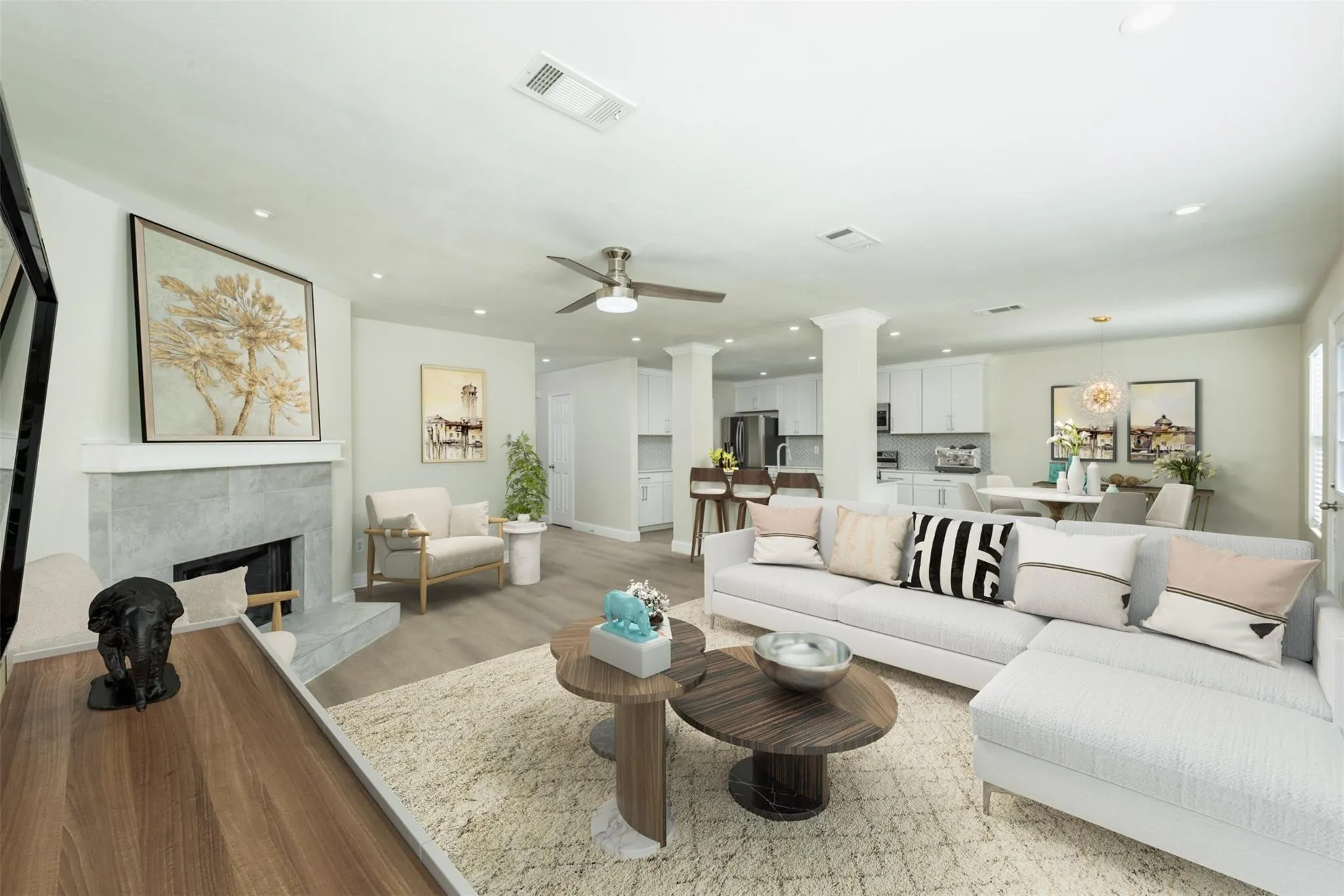 Living room with ceiling fan, decorative columns, light wood-type flooring, and a tiled fireplace