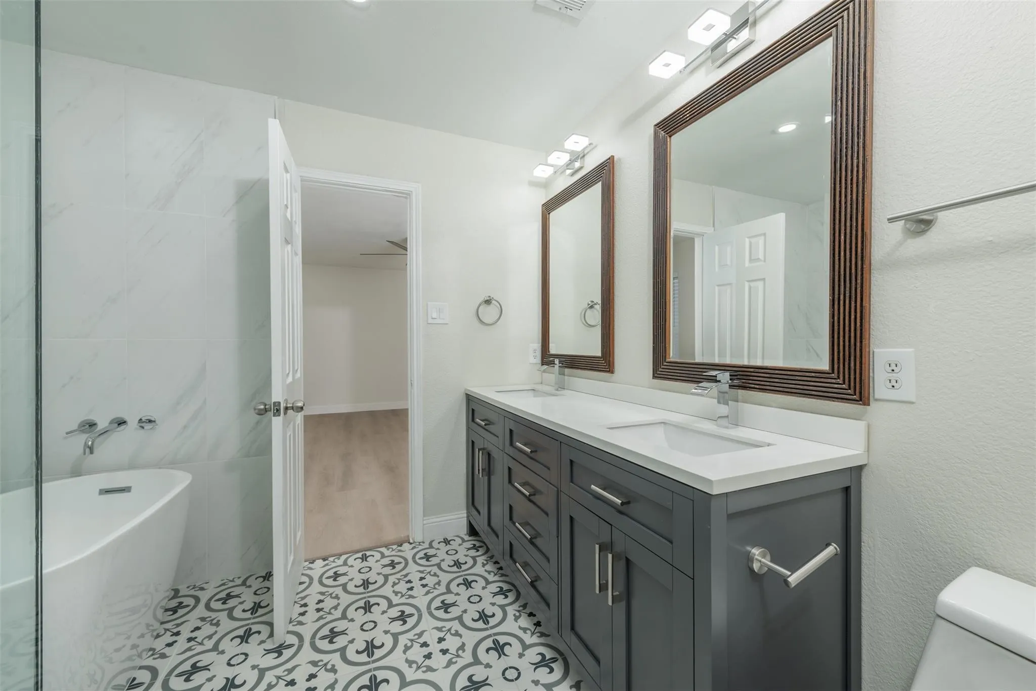 Bathroom with double vanity, a tub to relax in, toilet, and tile patterned floors