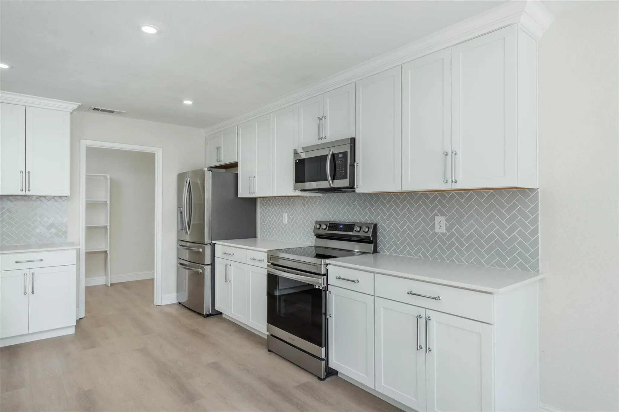 Kitchen featuring stainless steel appliances, light hardwood / wood-style flooring, white cabinetry, and decorative backsplash