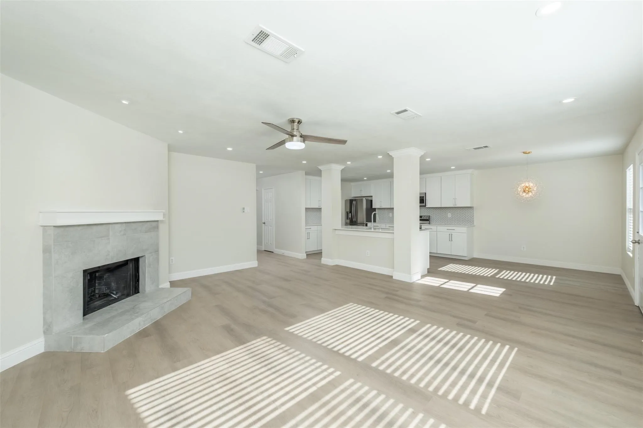 Unfurnished living room featuring a fireplace, light wood-type flooring, ornate columns, and ceiling fan