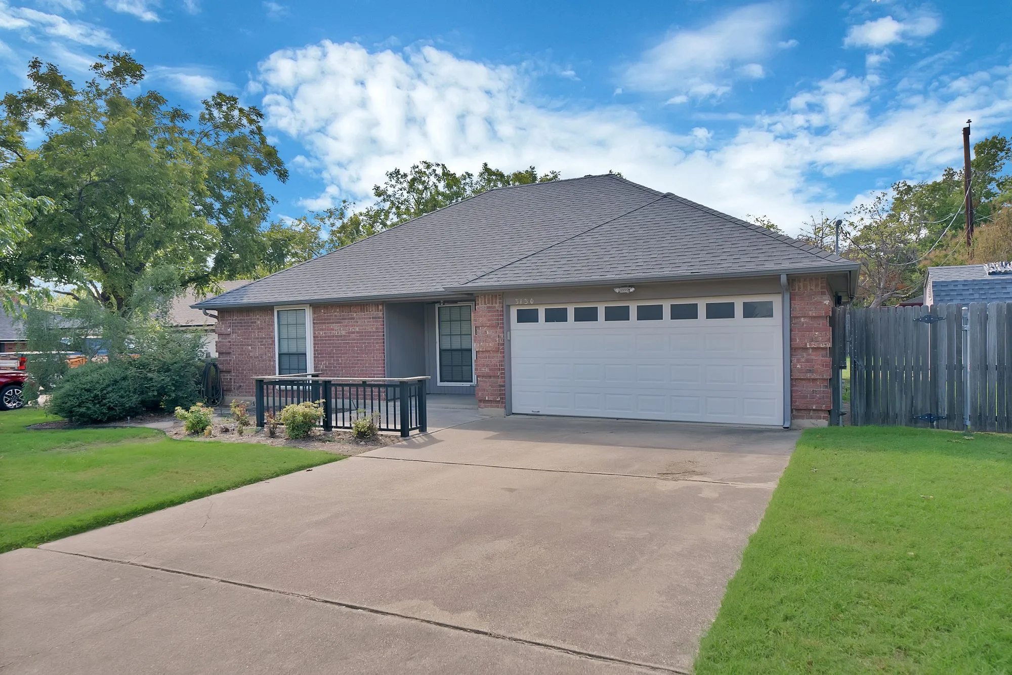 Brick exterior with a gray shingle roof, attached garage, concrete driveway, and front landscaping