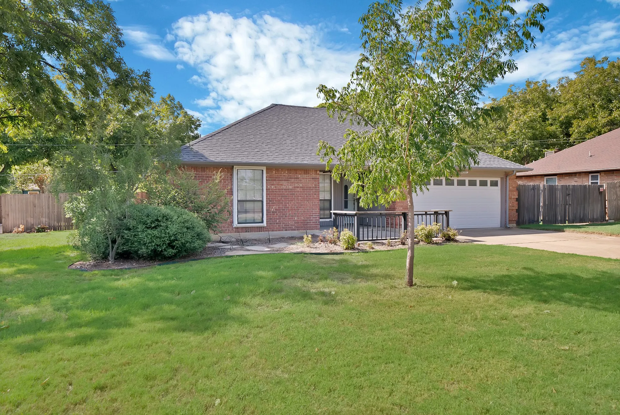 Brick exterior with a dark gray shingle roof, attached garage, and a covered porch with dark railings