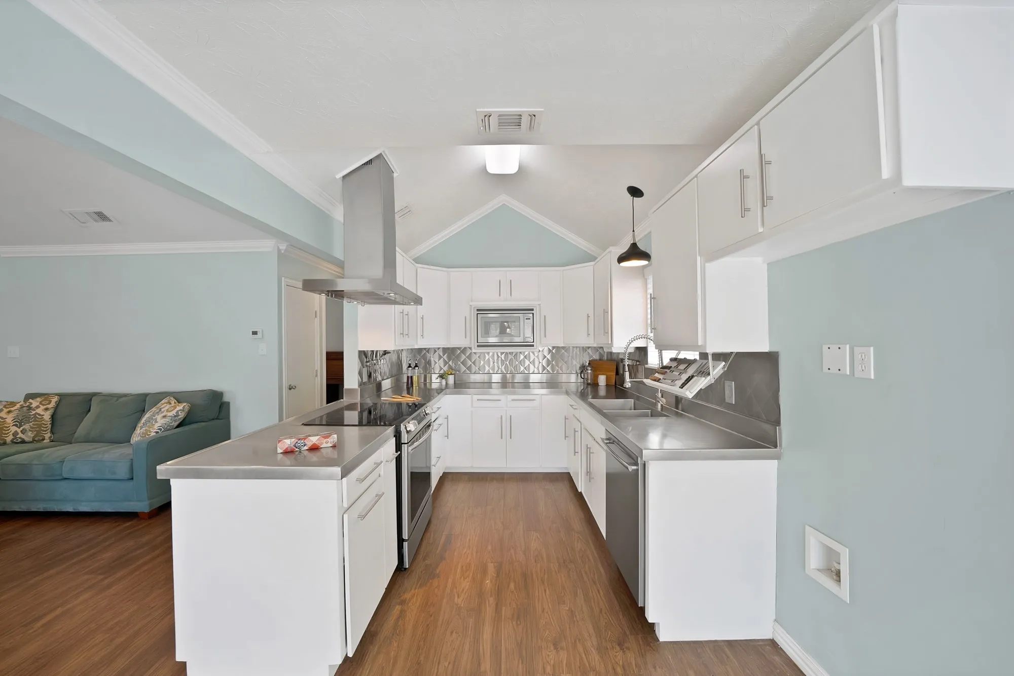 U-shaped kitchen featuring white cabinetry, stainless steel appliances, wood-finish flooring, and a vaulted ceiling