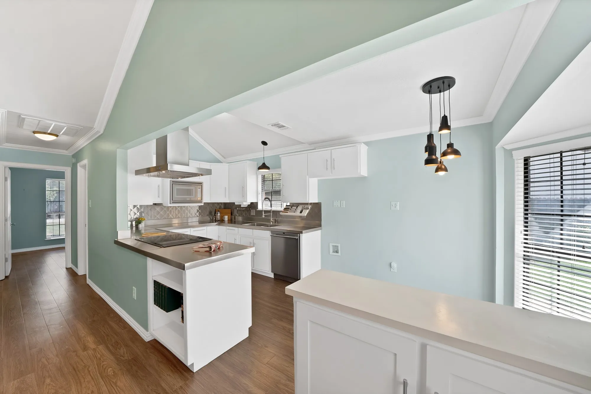 Kitchen featuring white cabinetry, stainless steel appliances, wood-finish flooring, and a decorative pendant light fixture