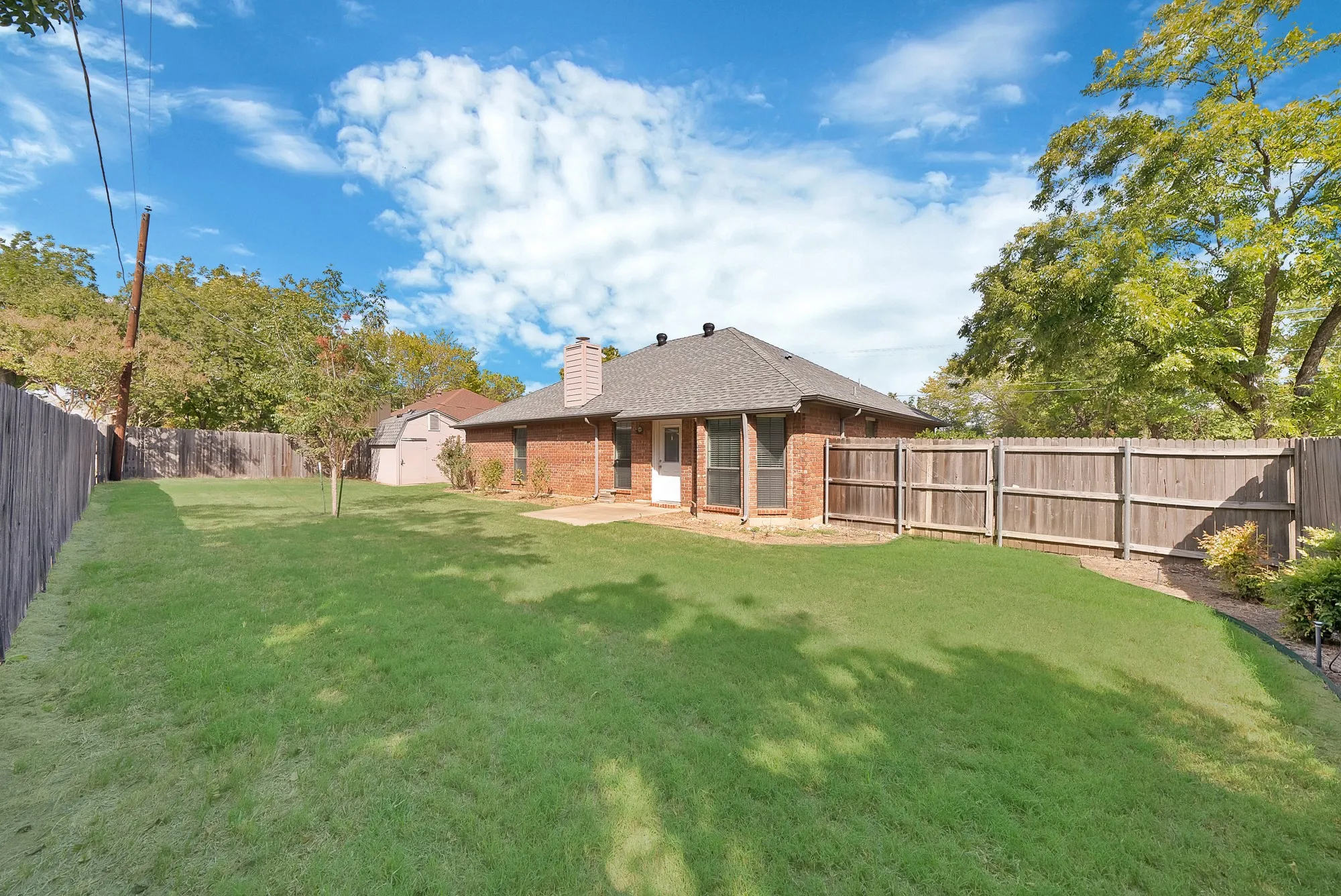 Expansive lawn area with a wood privacy fence, a brick exterior, and a shingle roof