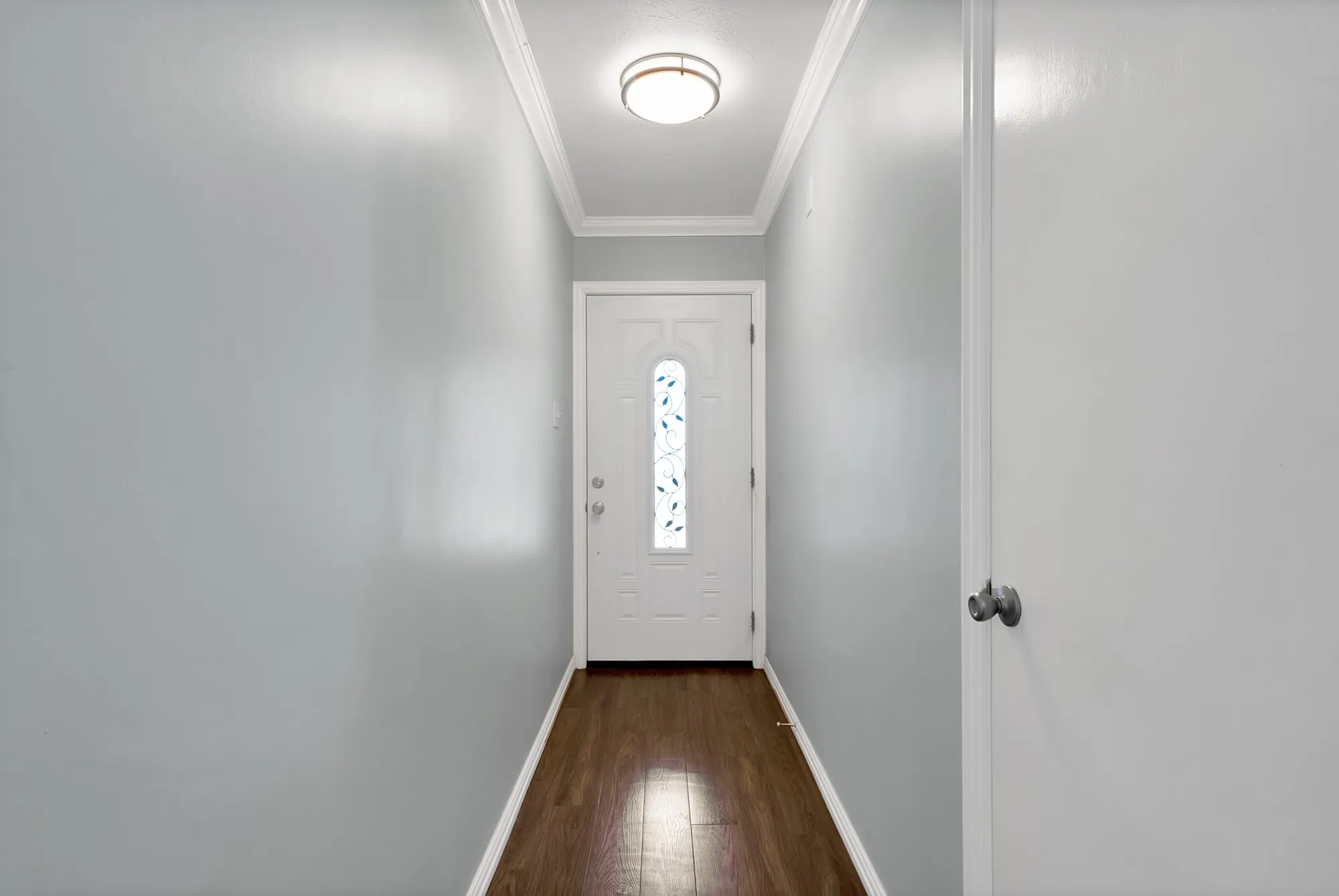Entryway featuring wood-finish flooring, light gray walls, and white crown molding