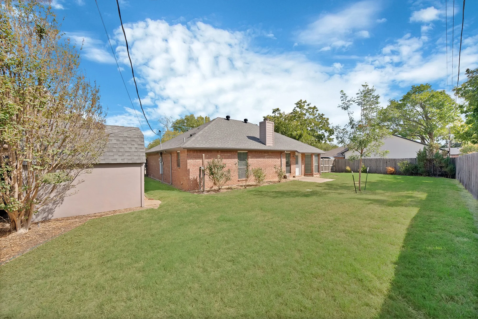 Expansive backyard featuring a manicured lawn, a detached storage building, a rear brick elevation, and a paved patio area