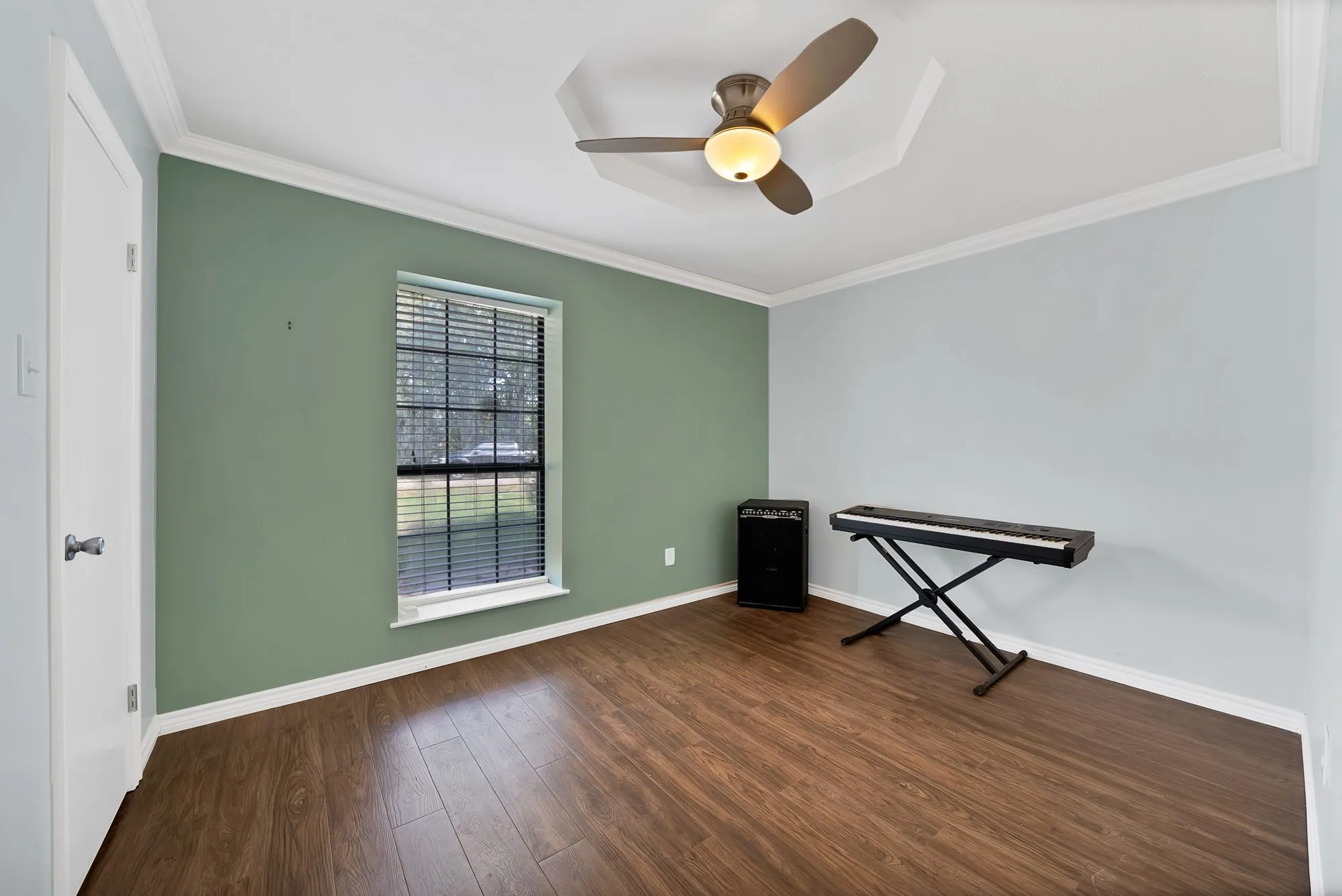 Wood-finish flooring, crown molding, a window with blinds, and a ceiling fan with integrated lighting