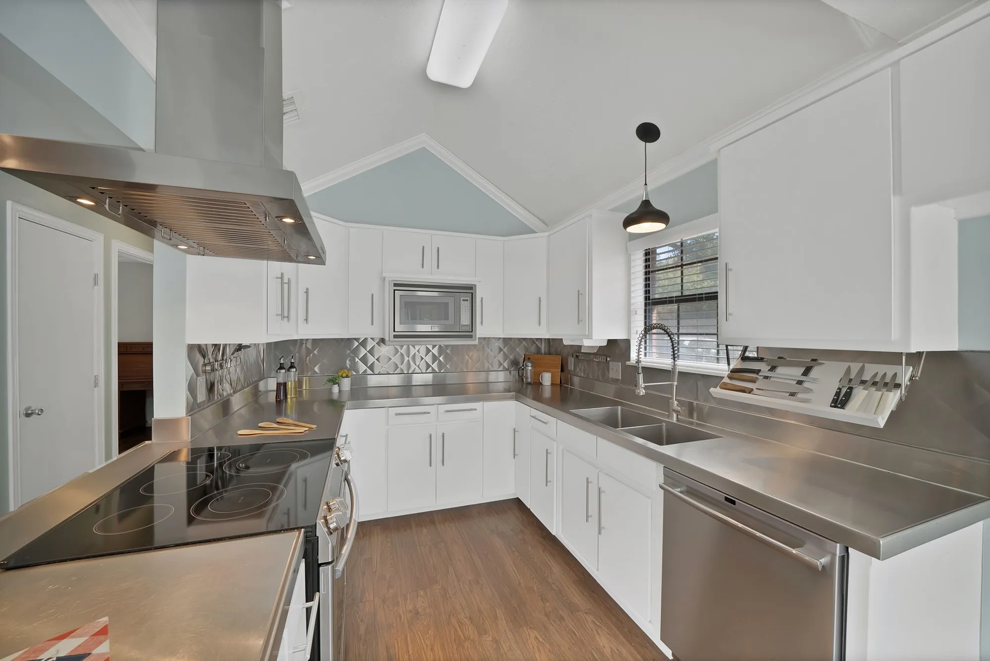 Kitchen featuring white cabinetry, stainless steel countertops, a stainless steel range hood, a double basin sink, and wood-finish flooring