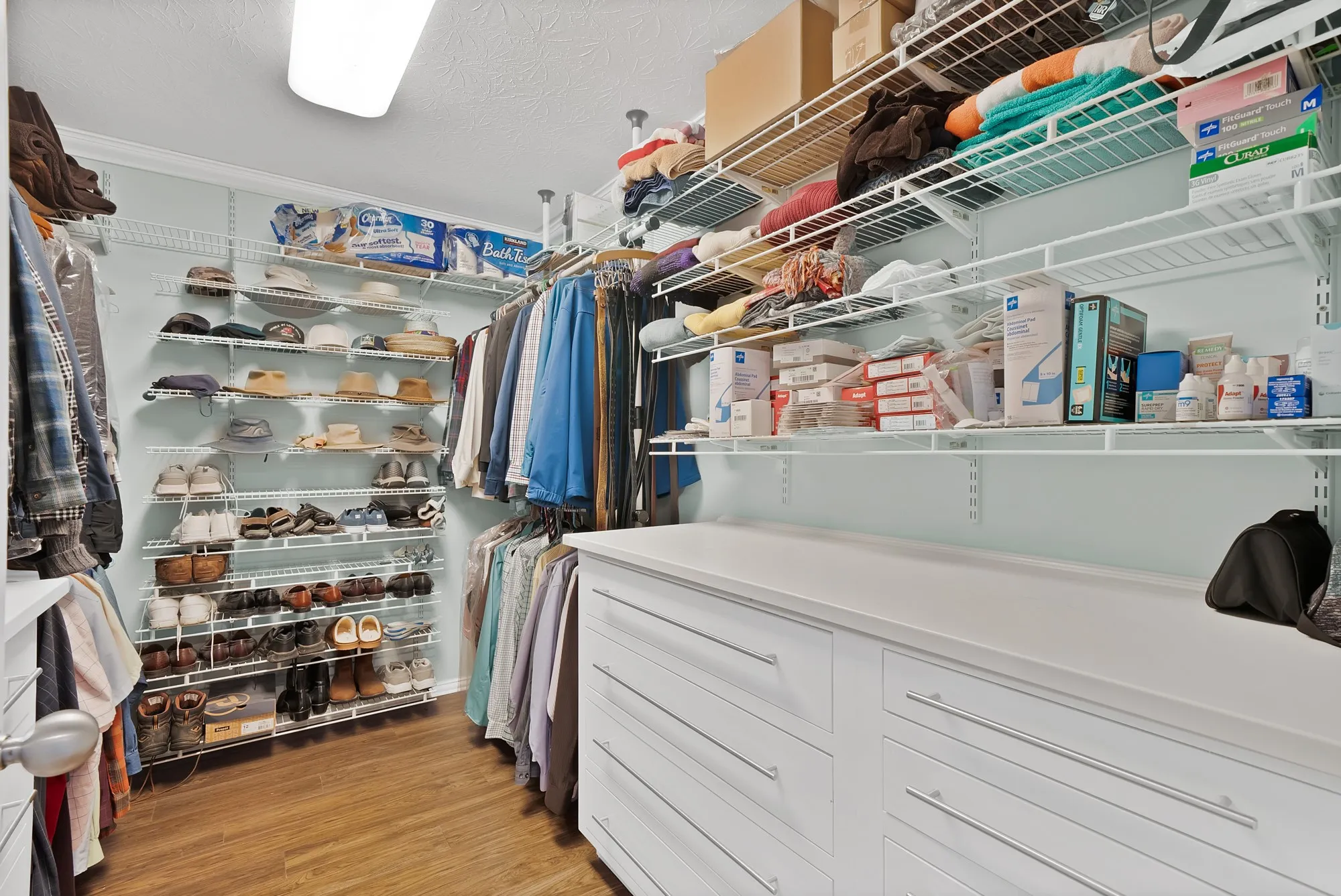 Closet featuring wood-finish flooring, white wire shelving, extensive hanging rods, and white built-in drawers