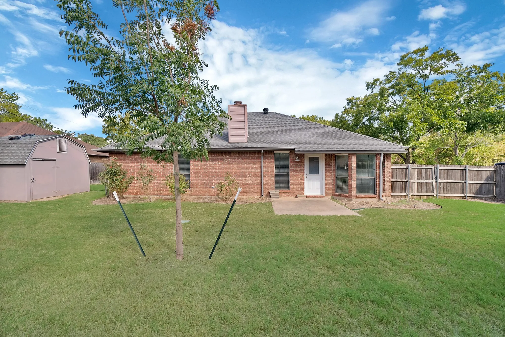 Expansive rear yard with a concrete patio, brick exterior, and a privacy fence
