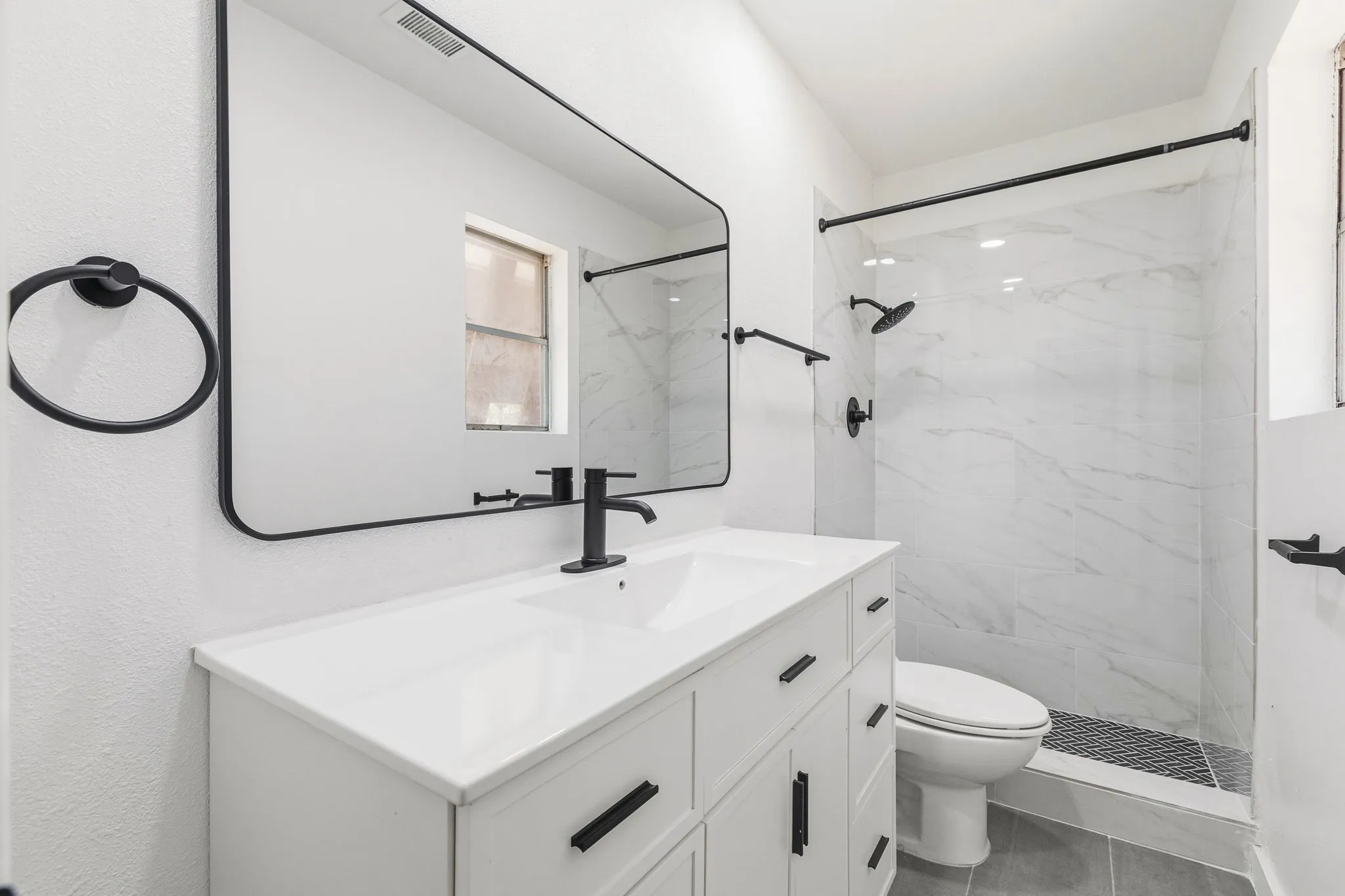 White vanity with integrated sink, matte black fixtures, and a frameless mirror