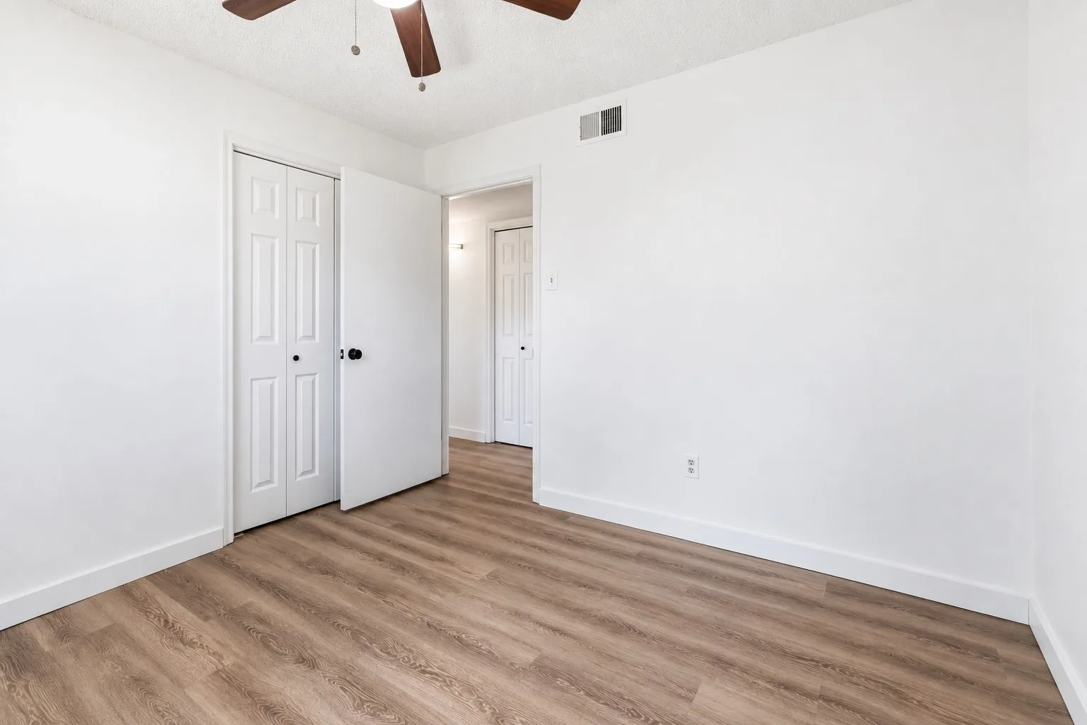 Wood-finish flooring, white walls, and a ceiling fan