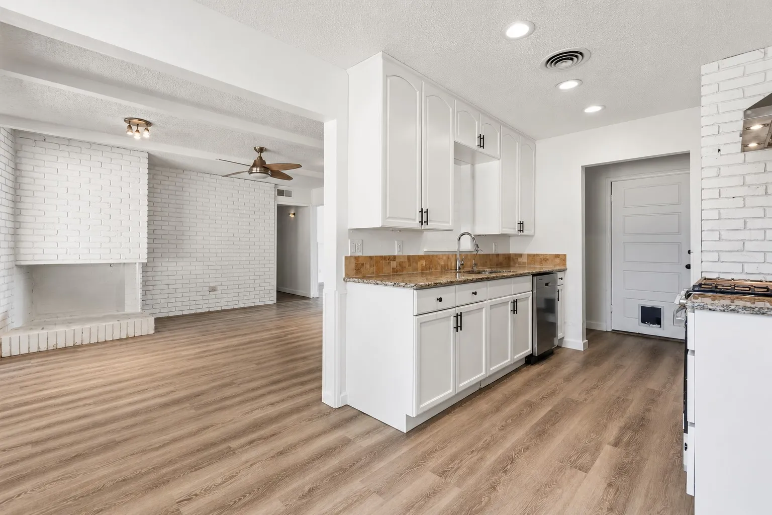 Kitchen featuring white cabinetry, a stainless steel dishwasher, an undermount sink, and speckled countertops