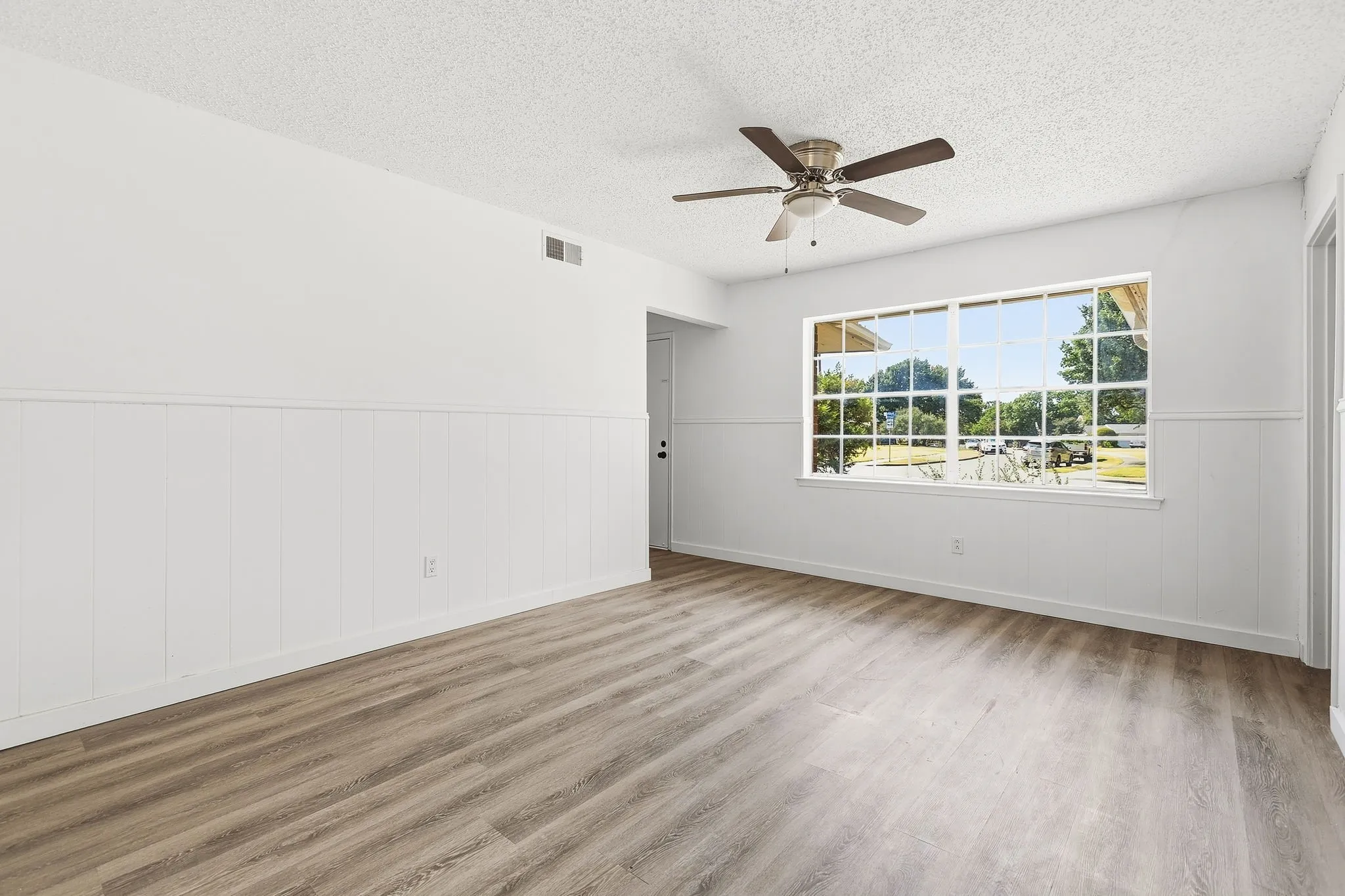 Wood-finish flooring with white wainscoting and a multi-pane window