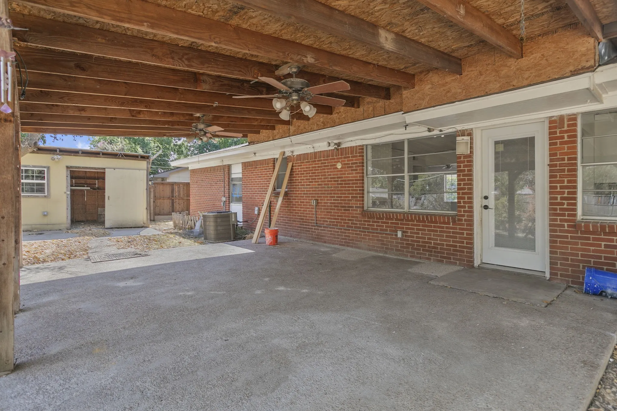Covered patio featuring exposed wood beams, dual ceiling fans, and a concrete slab