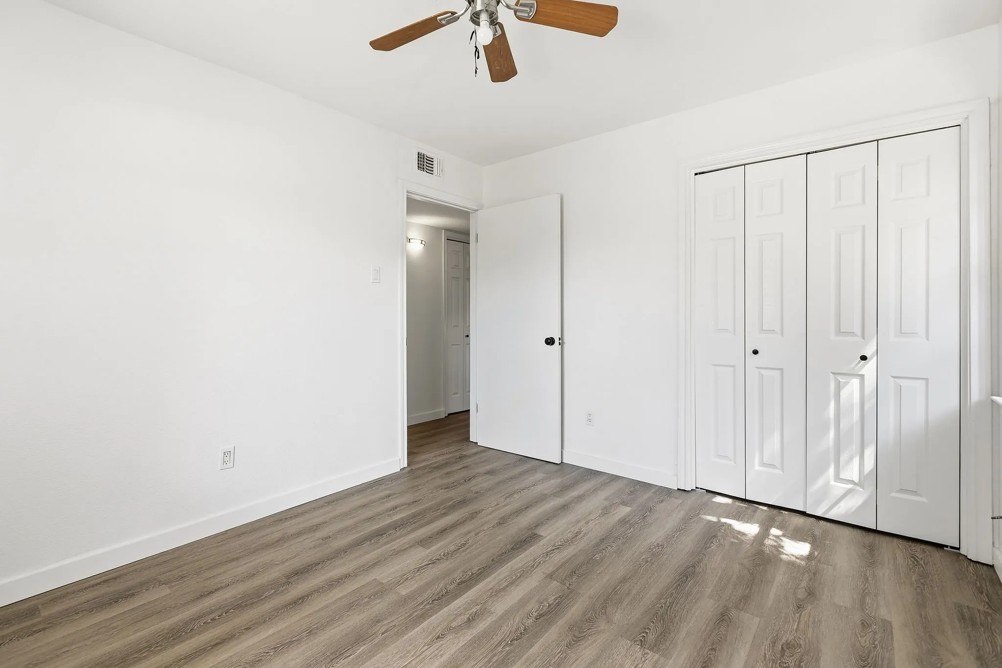 Spacious bedroom featuring wood-finish flooring, ceiling fan with light fixture, and abundant natural light