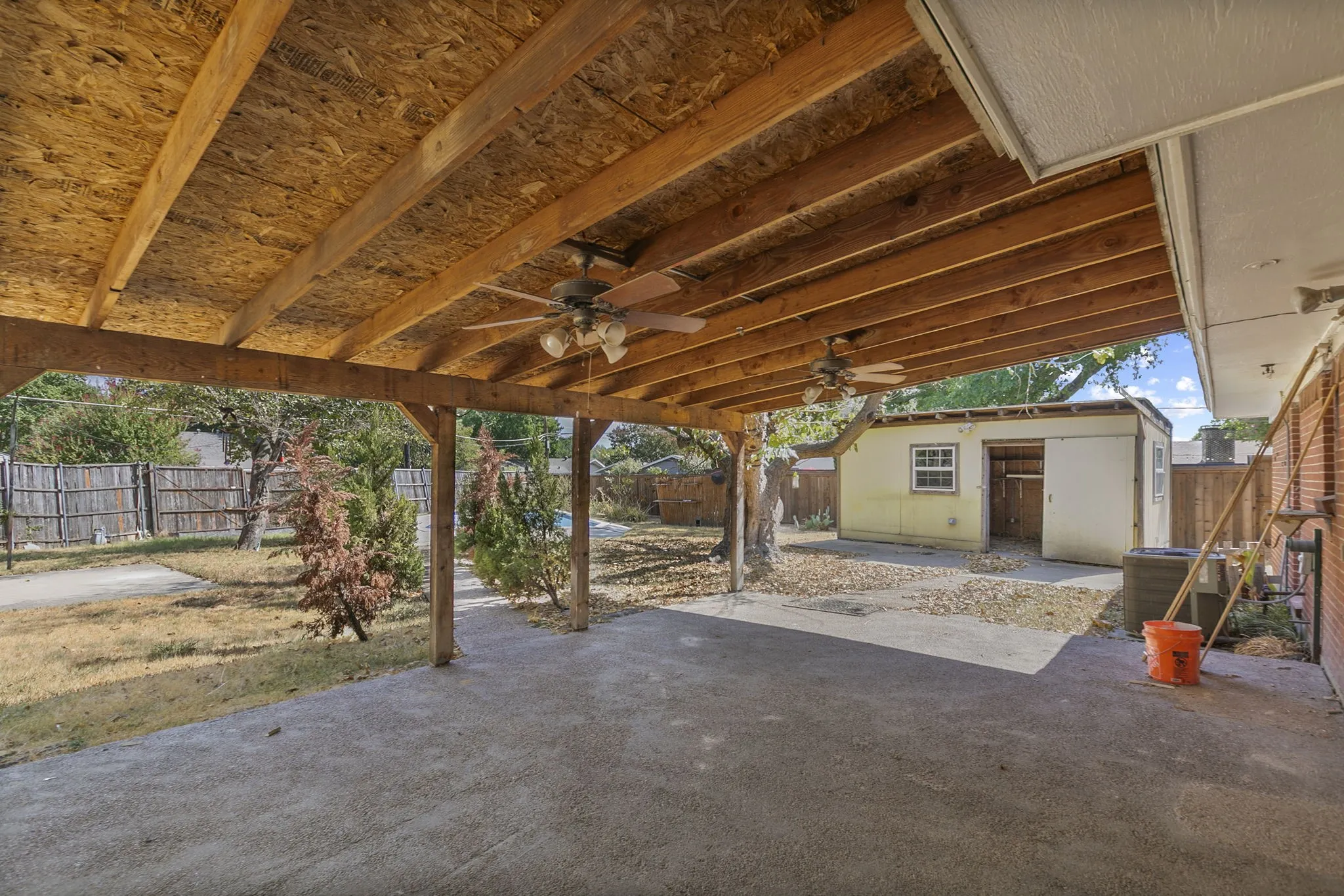 Covered patio with exposed wood beams, dual ceiling fans, and concrete flooring