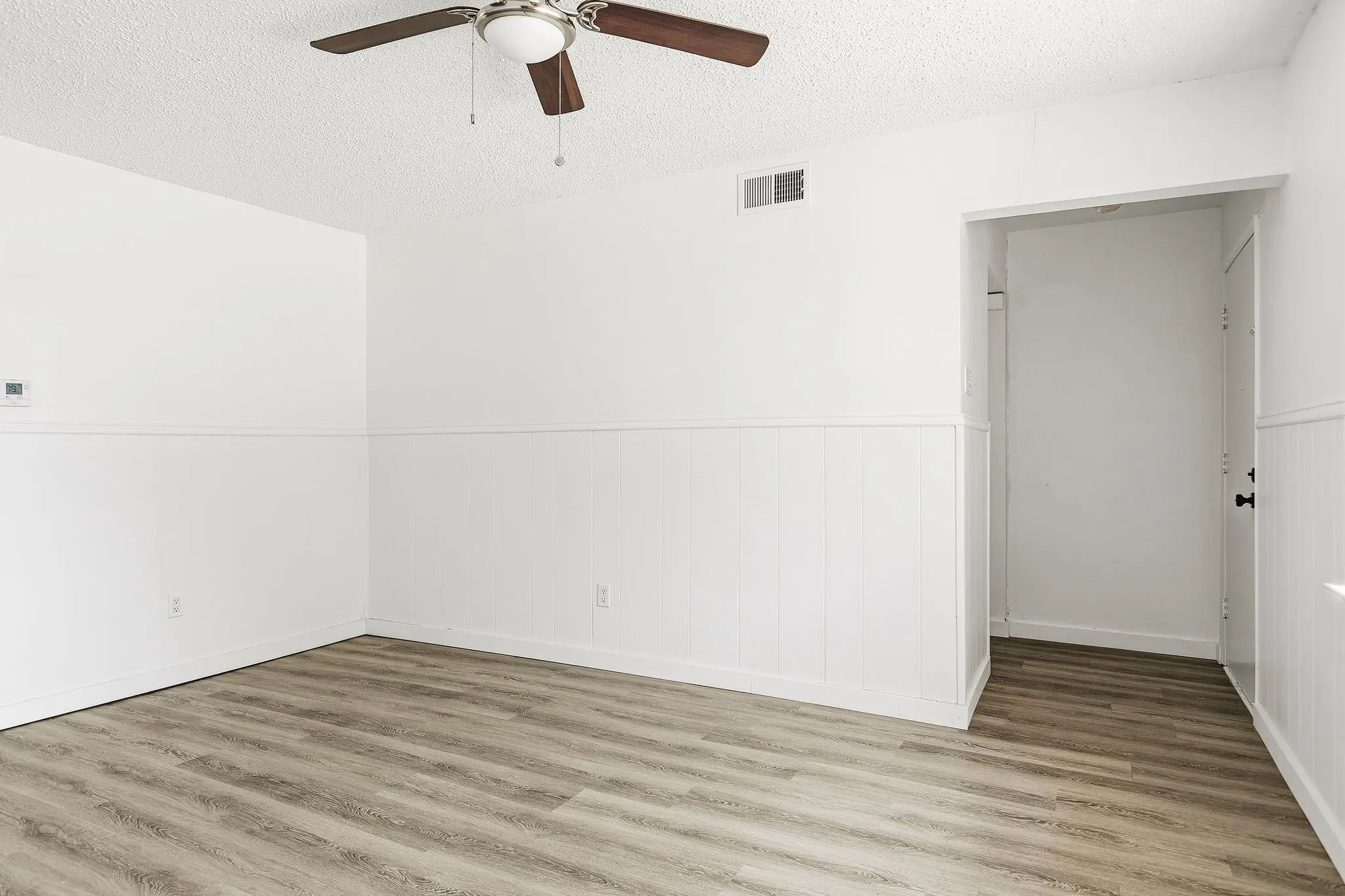 Wood-finish flooring, white beadboard wainscoting, white wall finishes, and a ceiling fan with light fixture