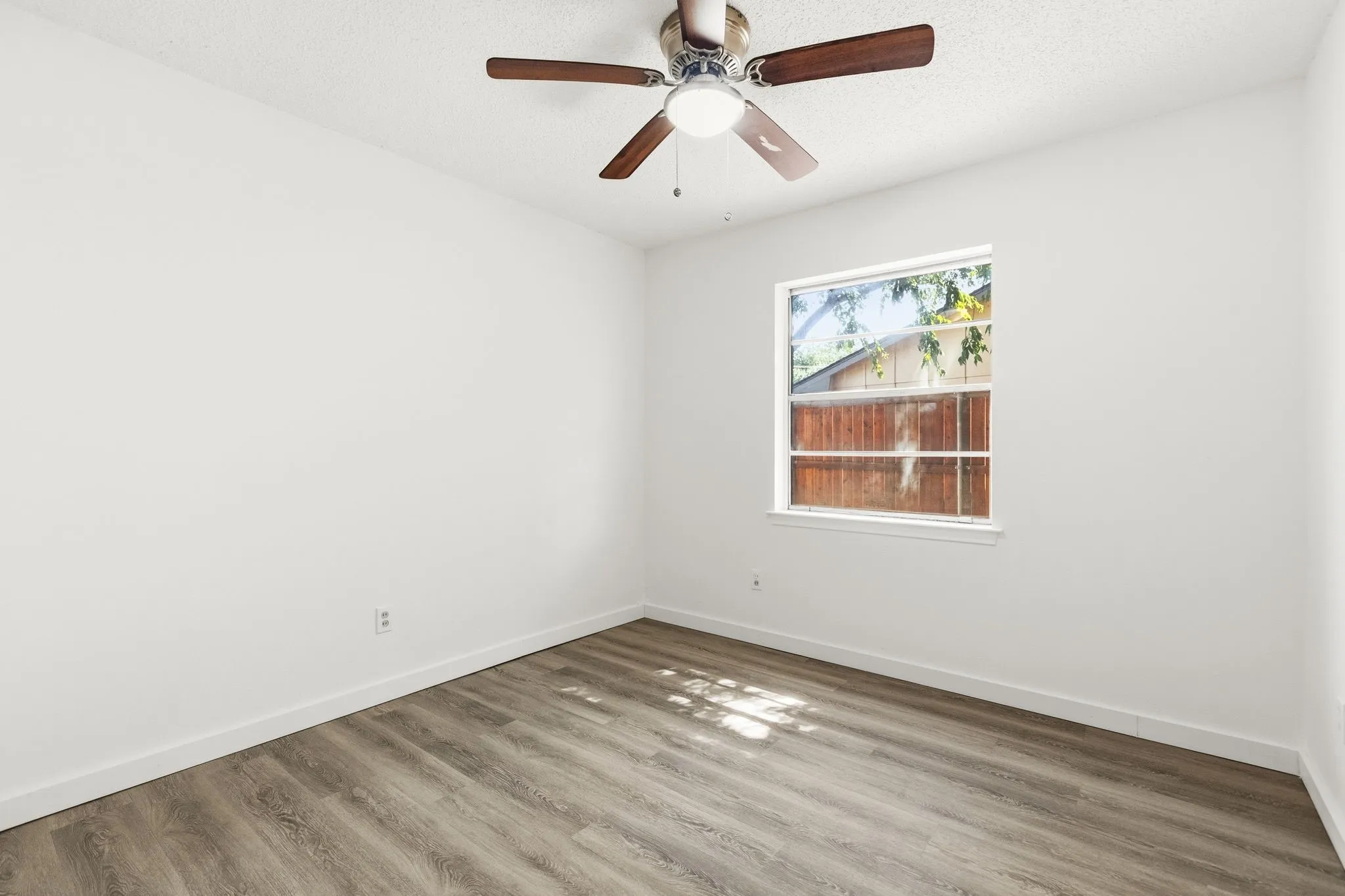 Wood-finish flooring with white baseboards, a window with white trim, a ceiling fan with integrated lighting, and white painted walls