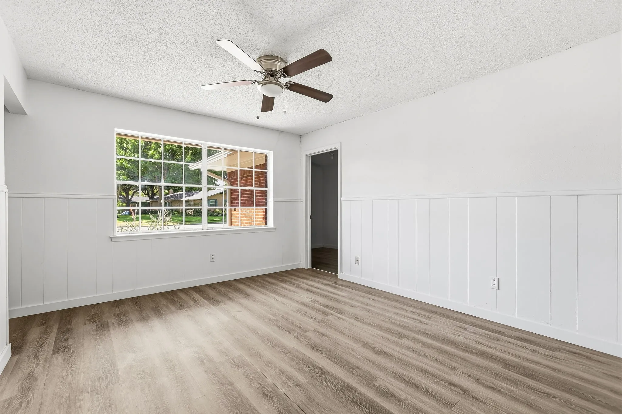 Wood-finish flooring, white paneled wainscoting, multi-pane window, and ceiling fan with integrated lighting