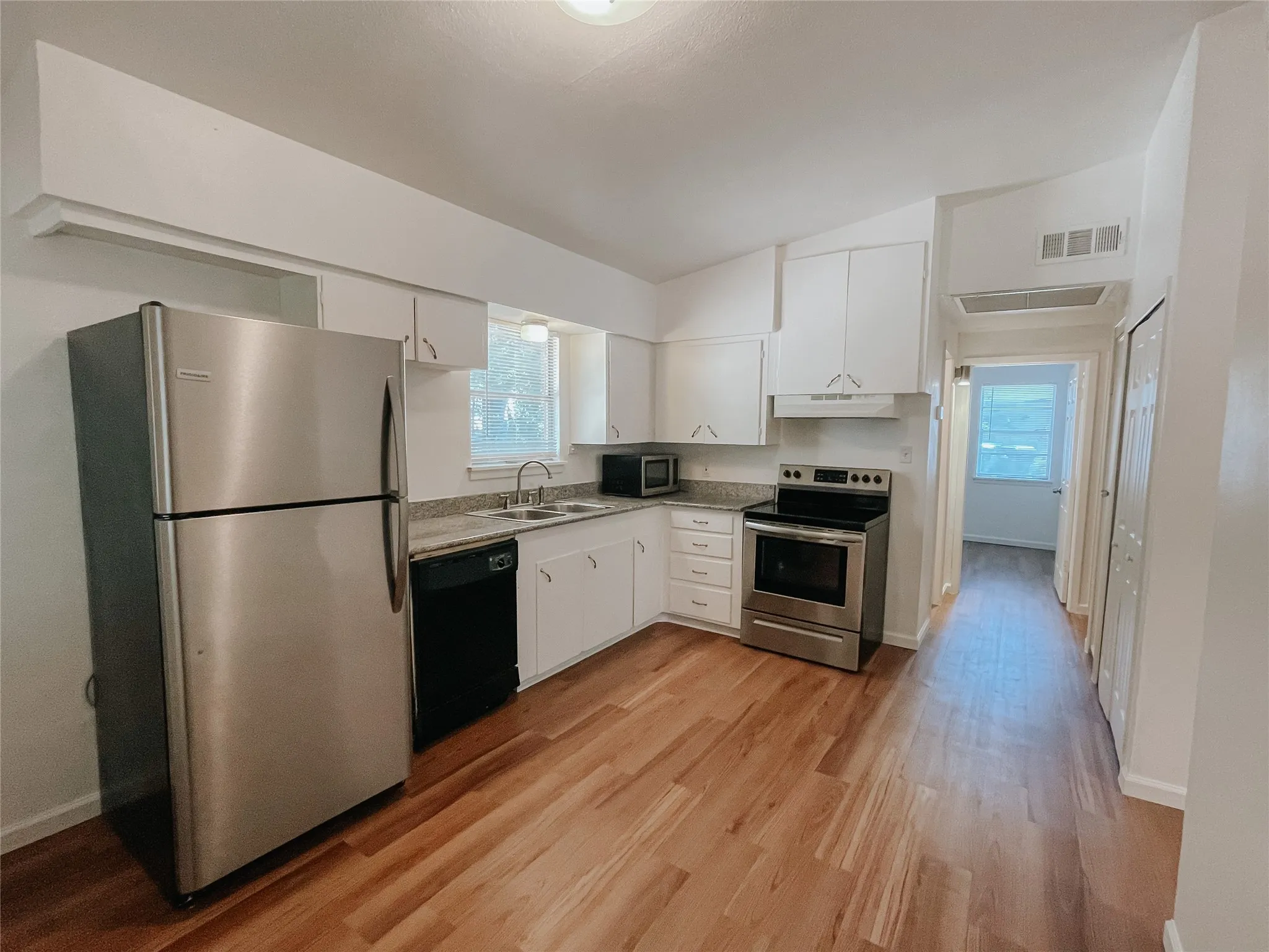 Kitchen featuring appliances with stainless steel finishes, light hardwood / wood-style flooring, white cabinets, sink, and a healthy amount of sunlight