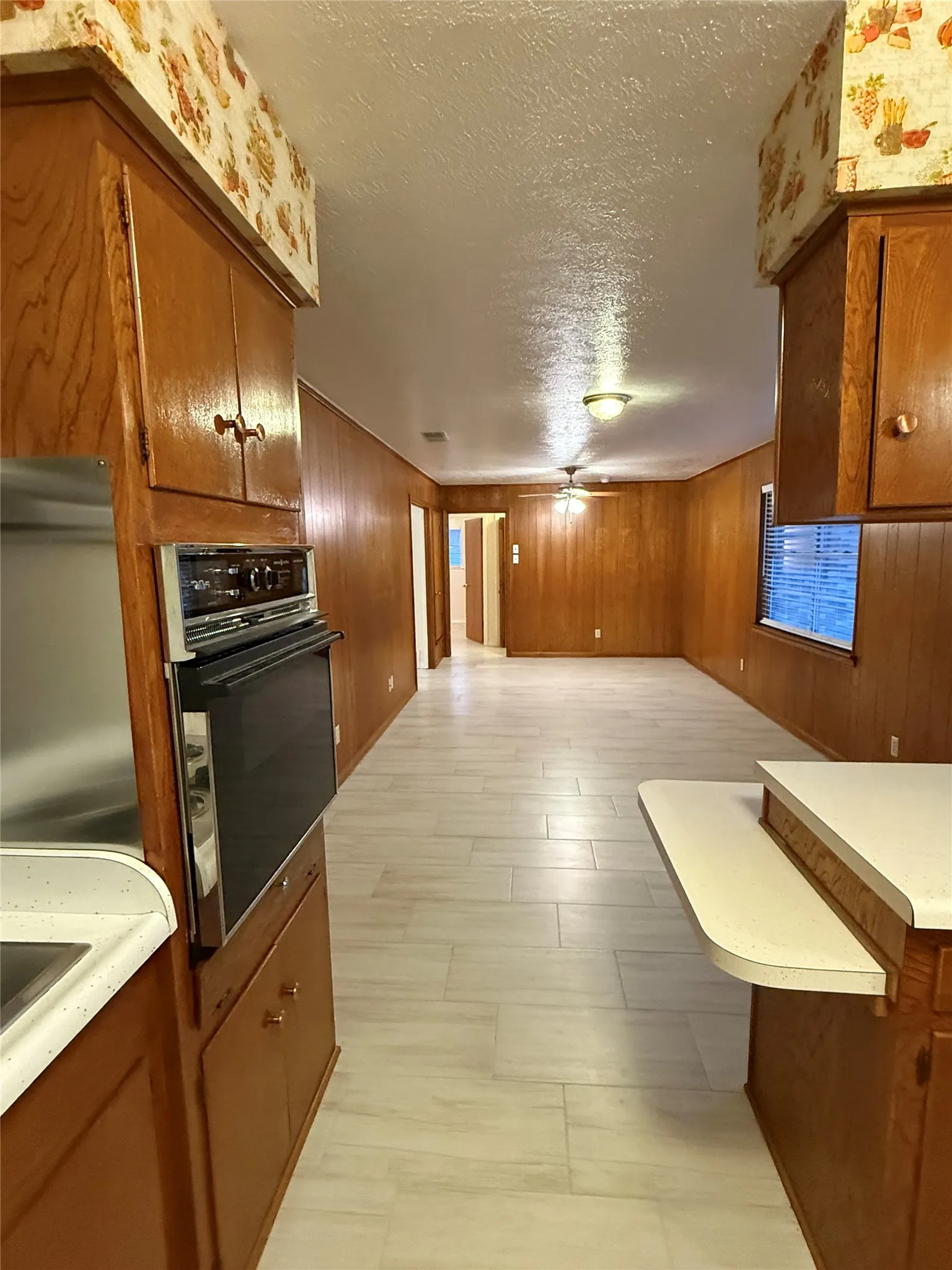 Kitchen featuring brown cabinets, wood walls, black oven, light countertops, and a textured ceiling