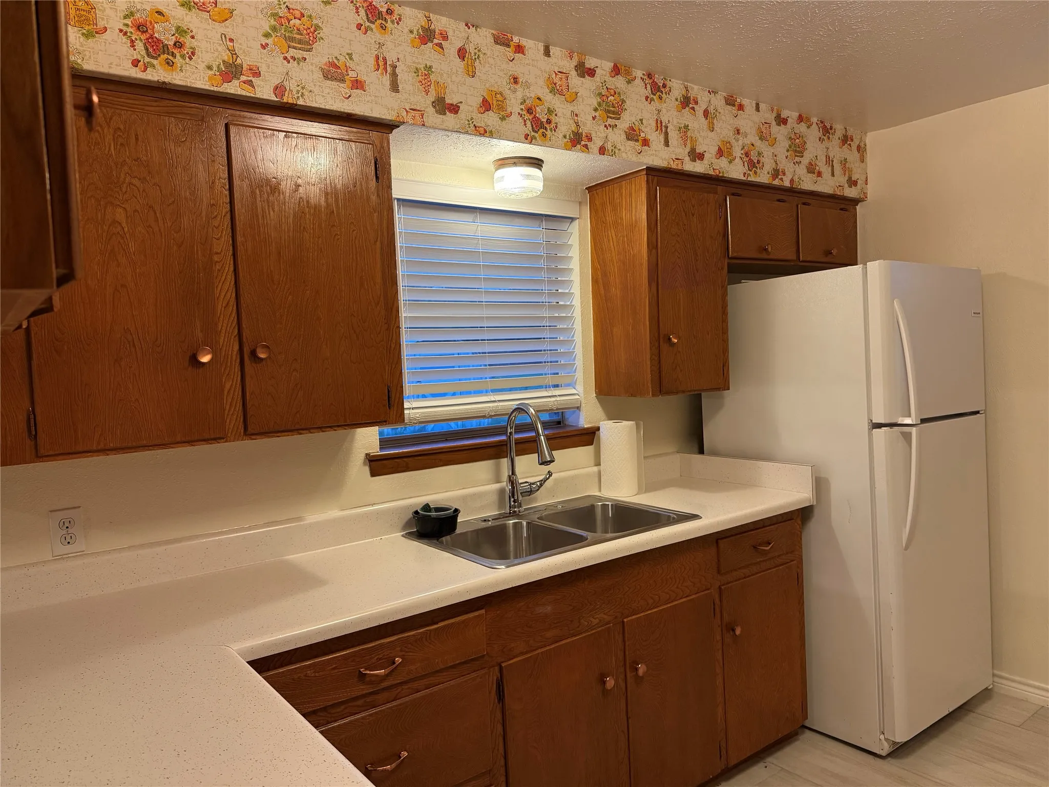 Kitchen featuring light countertops, freestanding refrigerator, brown cabinets, and a textured ceiling