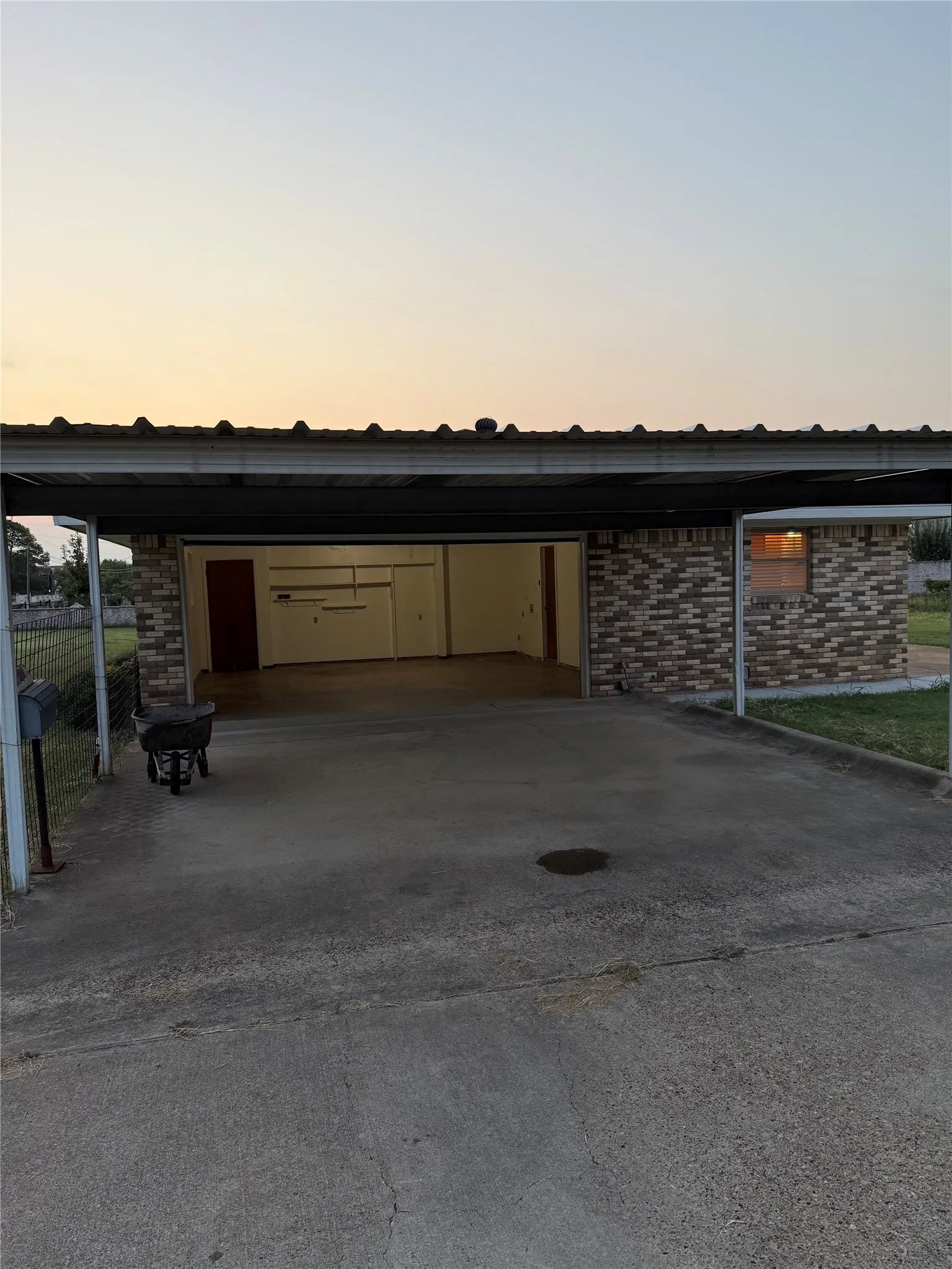 Garage at dusk with concrete driveway and a carport