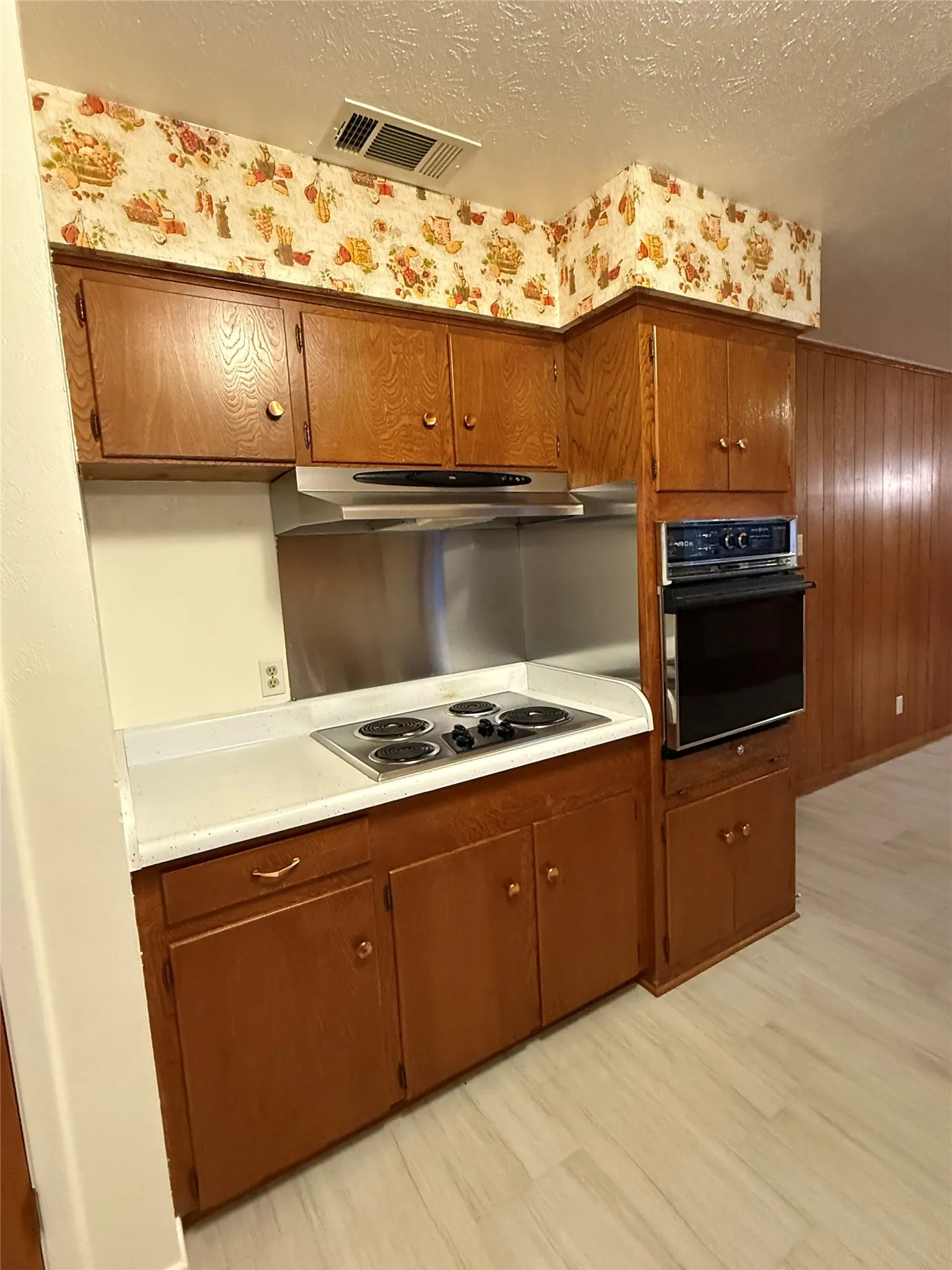 Kitchen with light countertops, oven, a textured ceiling, wood walls, and stainless steel electric cooktop