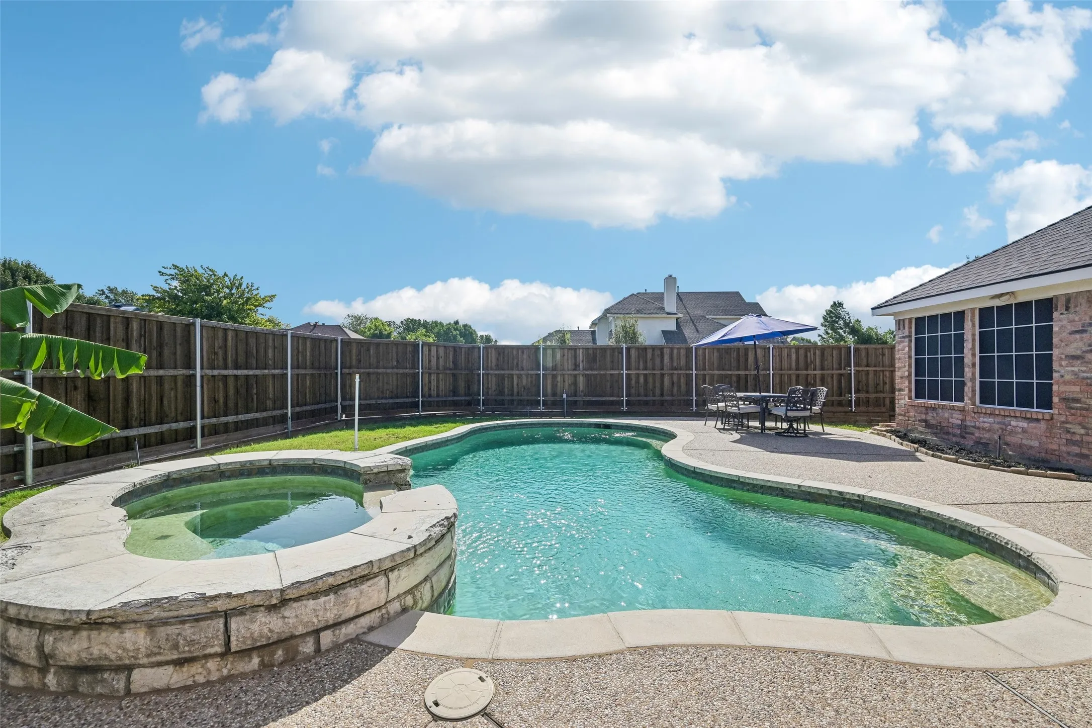 Expansive backyard featuring a custom-shaped pool, integrated spa with stone surround, and an exposed aggregate patio