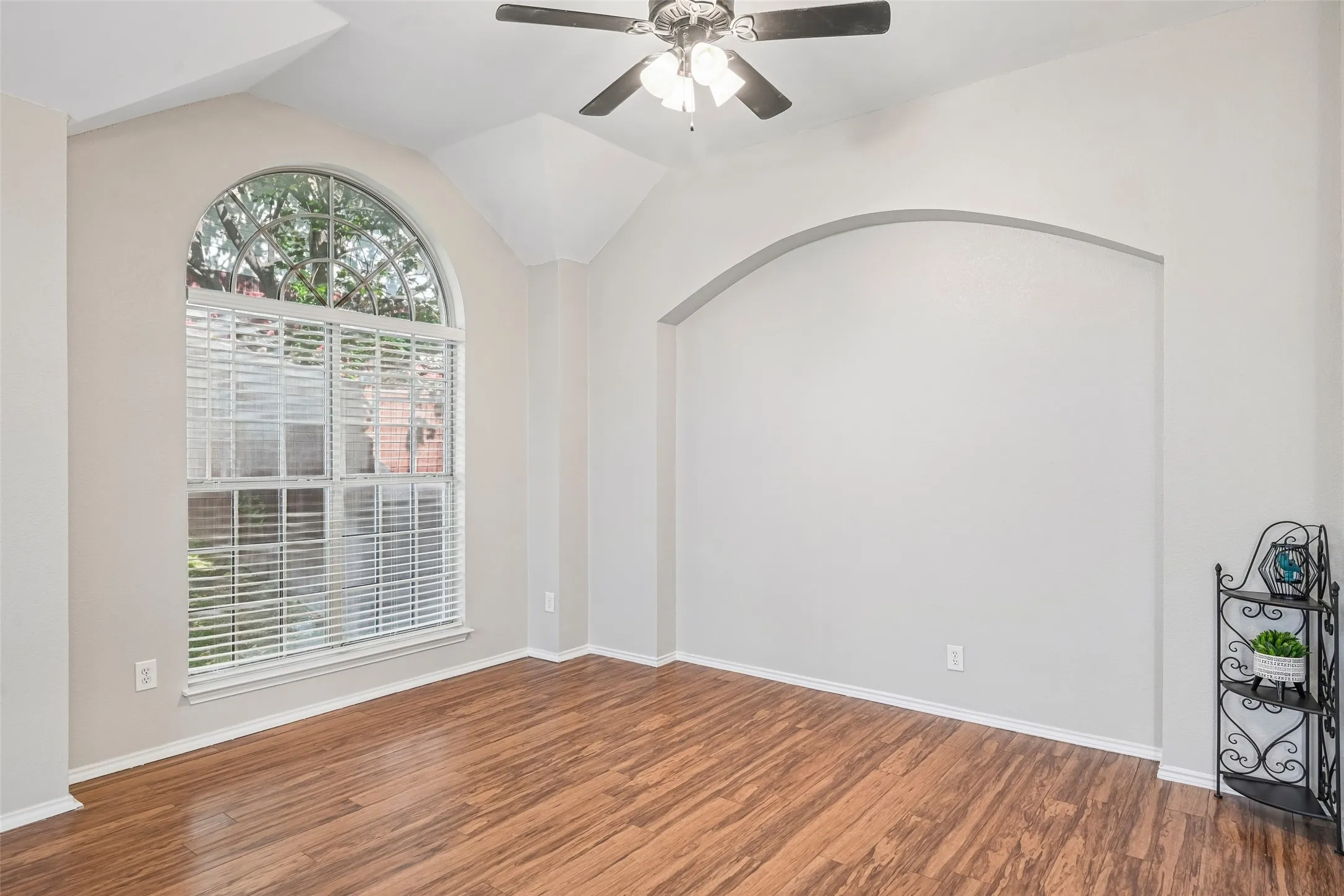 Arched window with blinds, vaulted ceiling, ceiling fan, and an arched wall niche