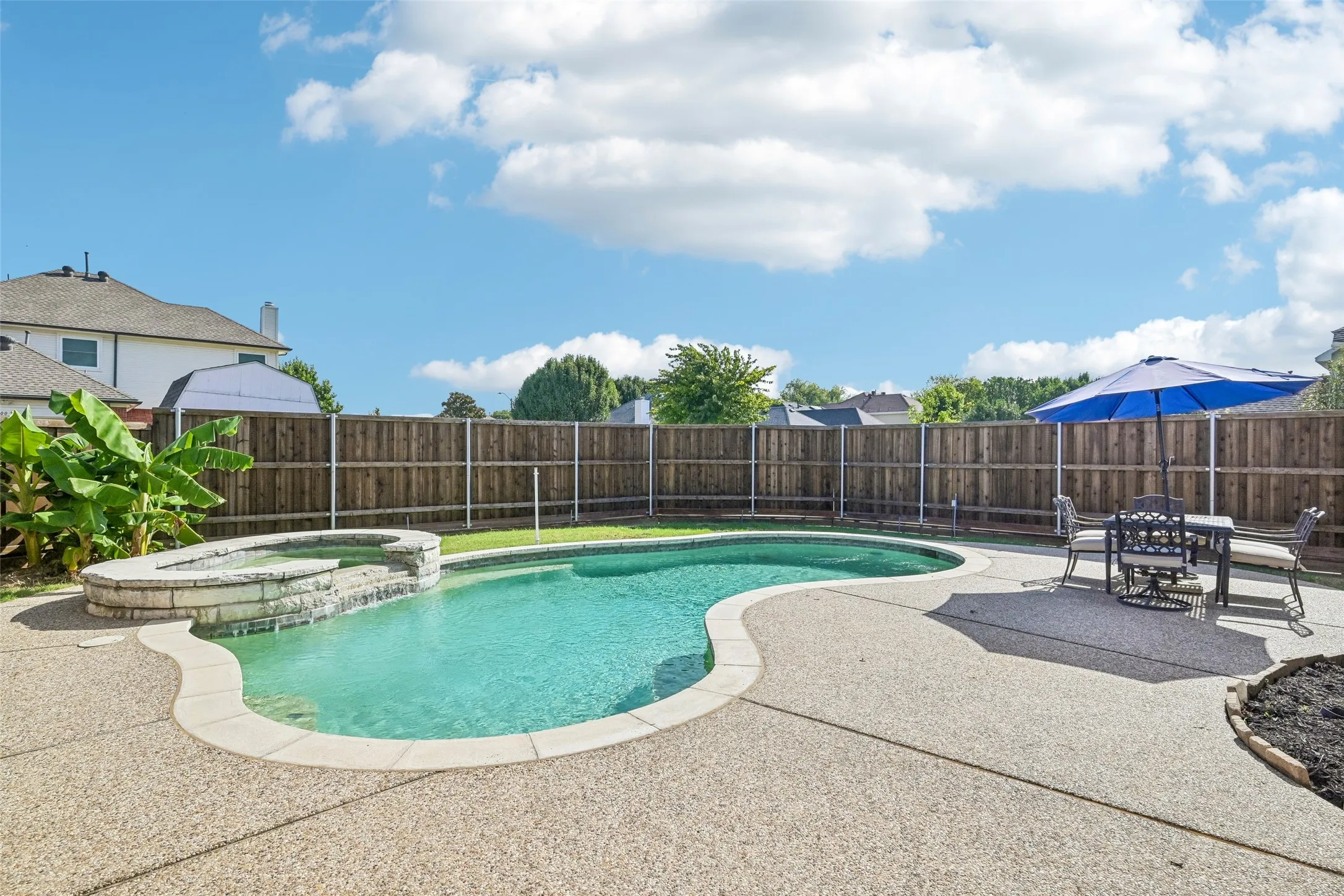Resort-style backyard featuring a freeform swimming pool, integrated spa with stone surround, and extensive concrete decking