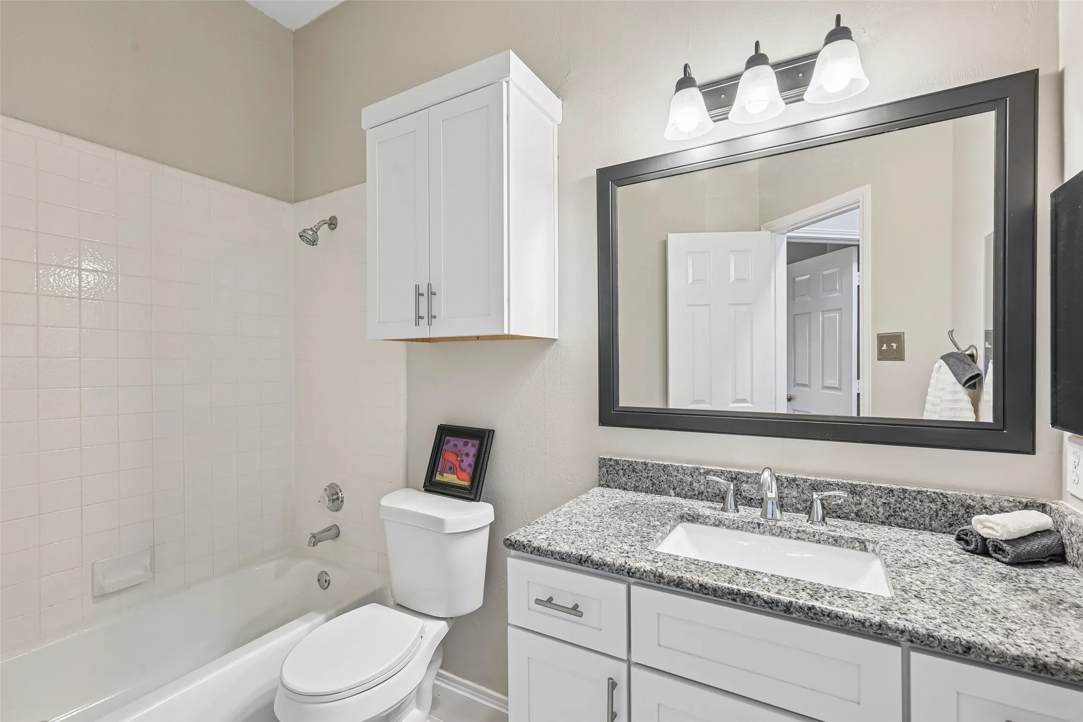 White vanity with granite countertop, undermount sink, and polished chrome faucet