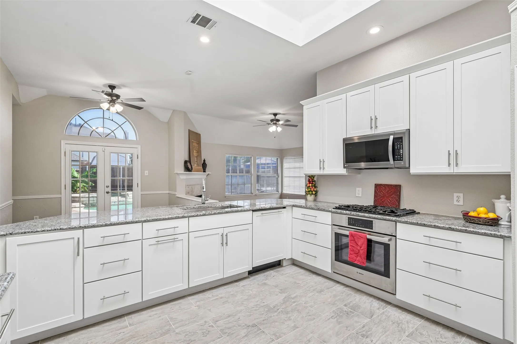 Kitchen featuring white shaker cabinetry, granite countertops, tile flooring, stainless steel appliances, and a vaulted ceiling with recessed lighting
